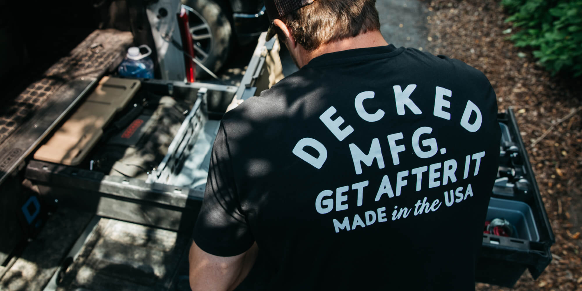 Person wearing a black t-shirt with 'Decked MFG.' branding outdoors.