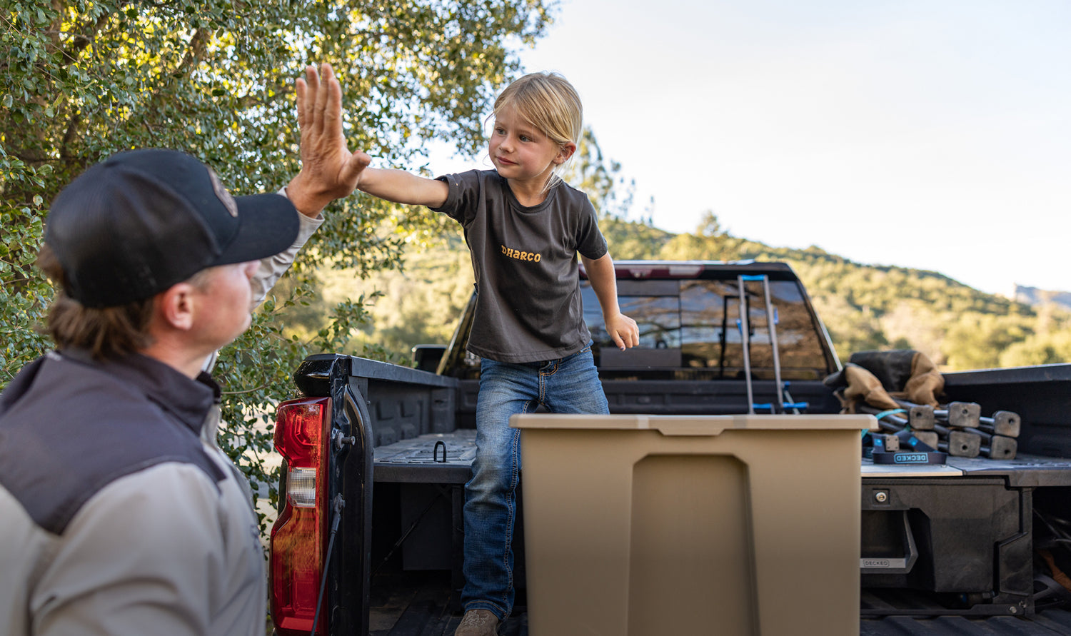 Person and child giving high-five in a truck bed with a scenic background