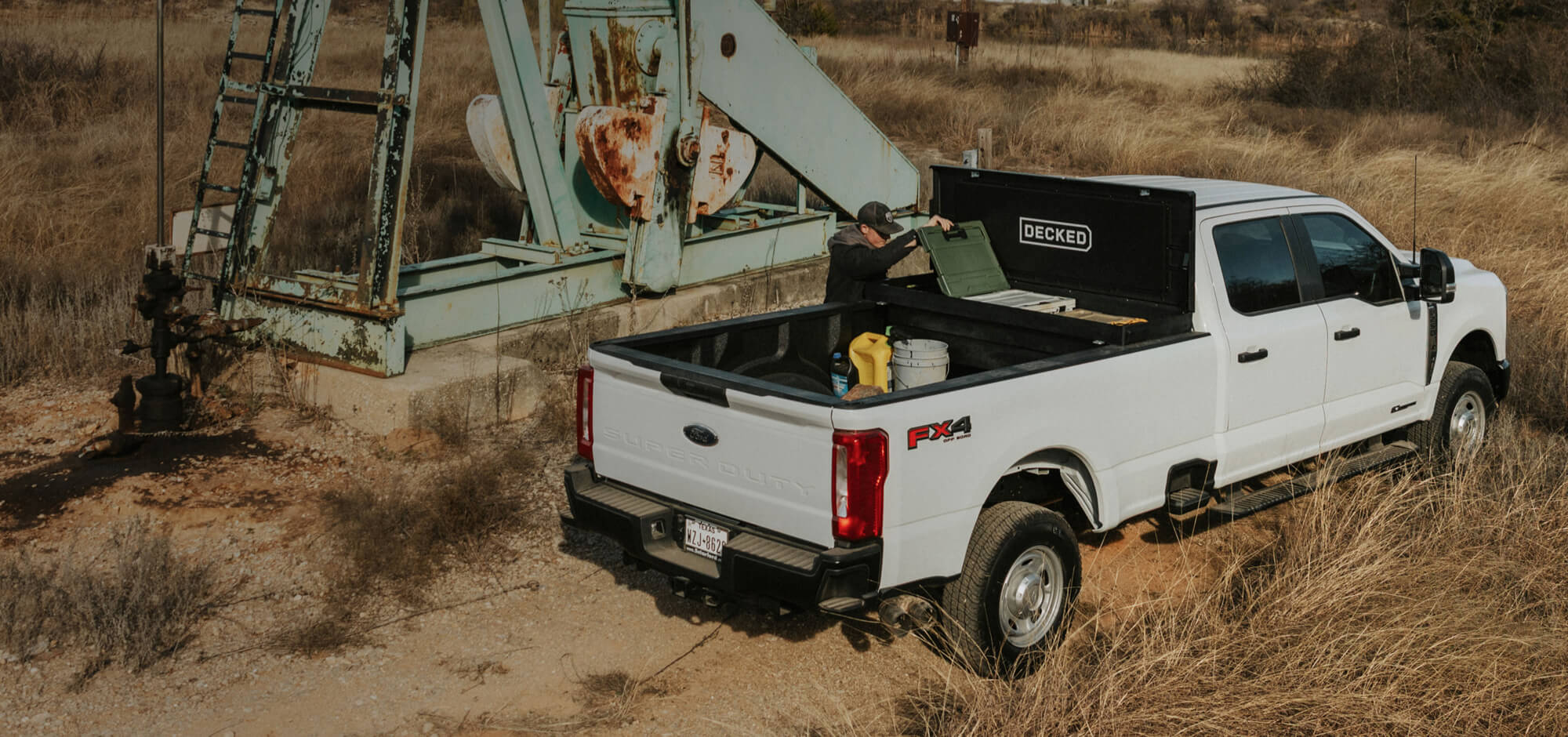 White pickup truck with a toolbox in a desert setting near an oil pumpjack.