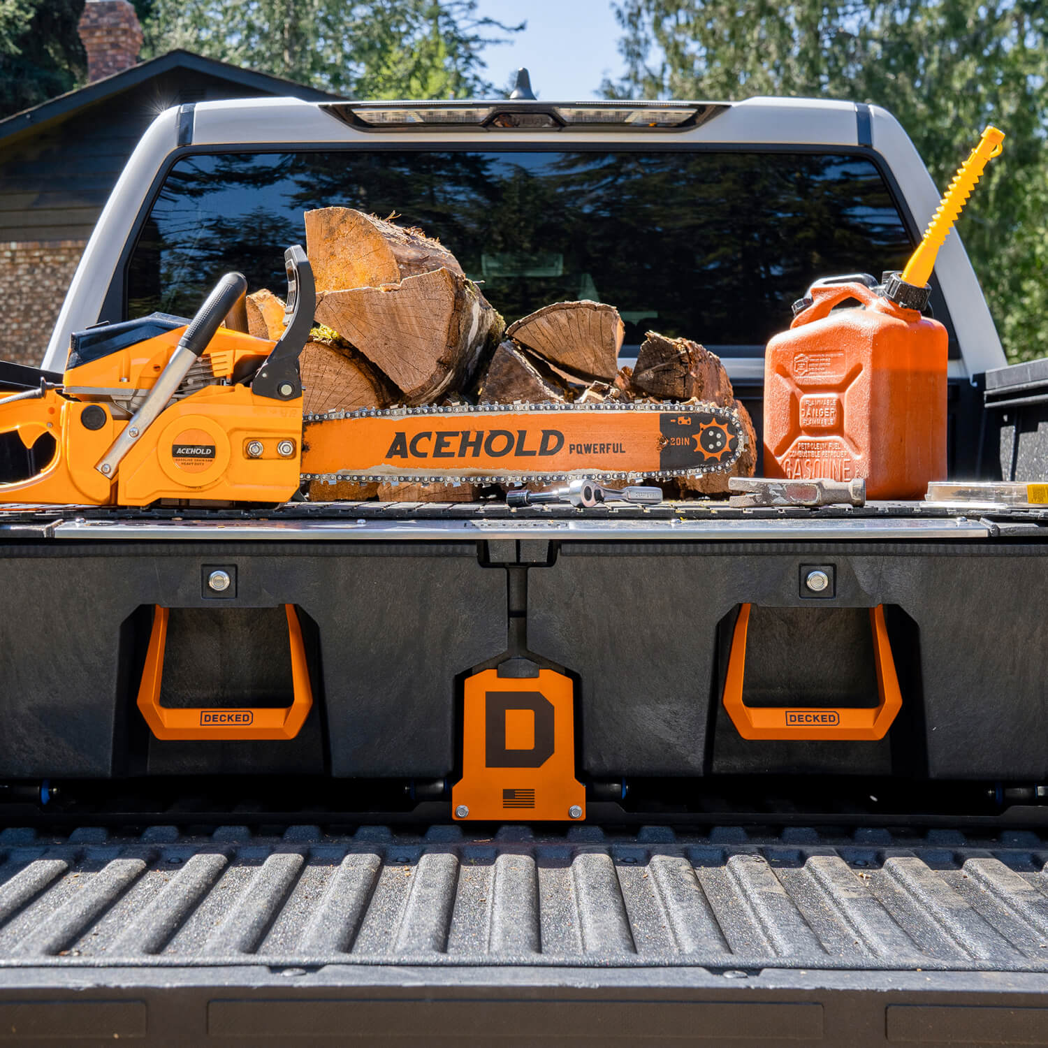 Truck bed with logs, chainsaw, and gas canister sitting on top of a DECKED Drawer System with the Orange Hop-Up Kit handles and center COD piece.
