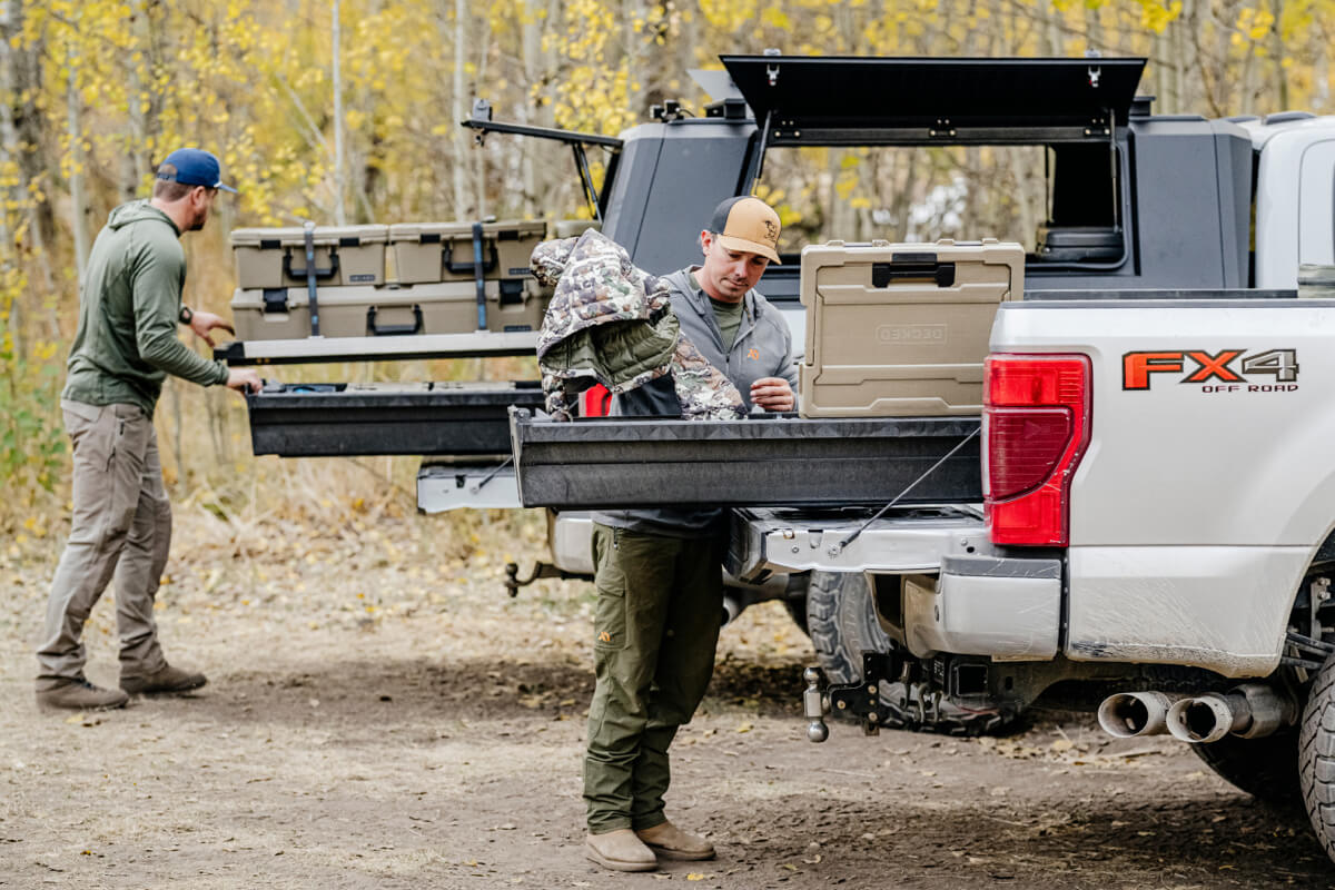 Two men loading a truck bed's Drawer System with camping gear in a forest setting