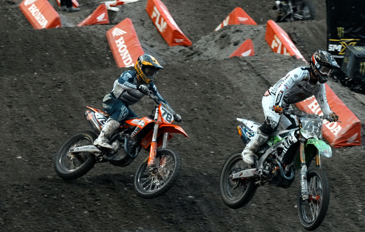 Two motocross riders on a dirt track with Honda branding.