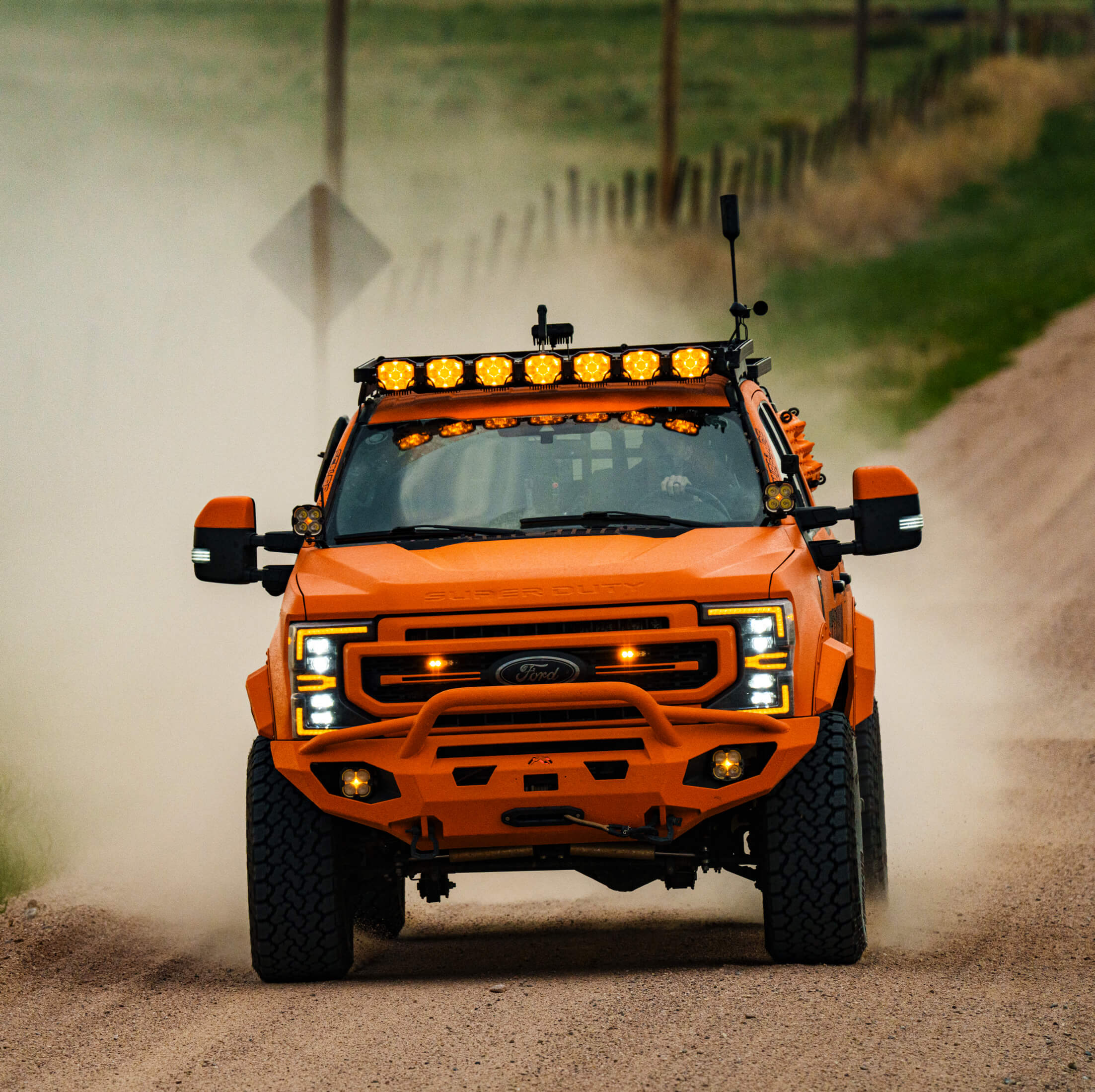Orange off-road vehicle driving on a dirt road with dust in the air