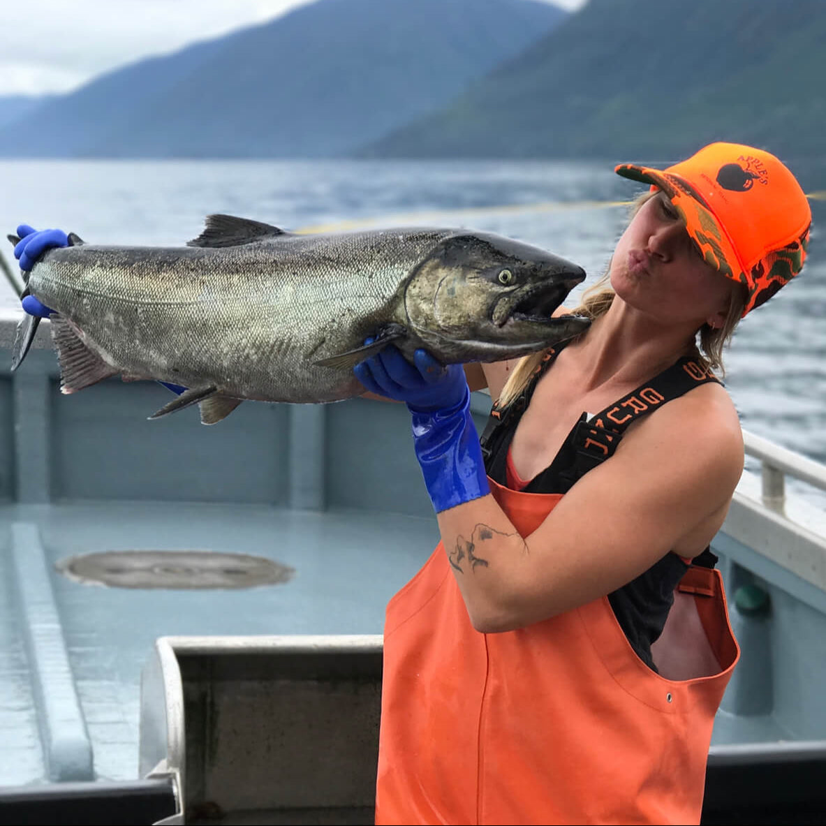 McKenna on deck of a fishing boat in Alaska, holding a salmon up for a smooch.