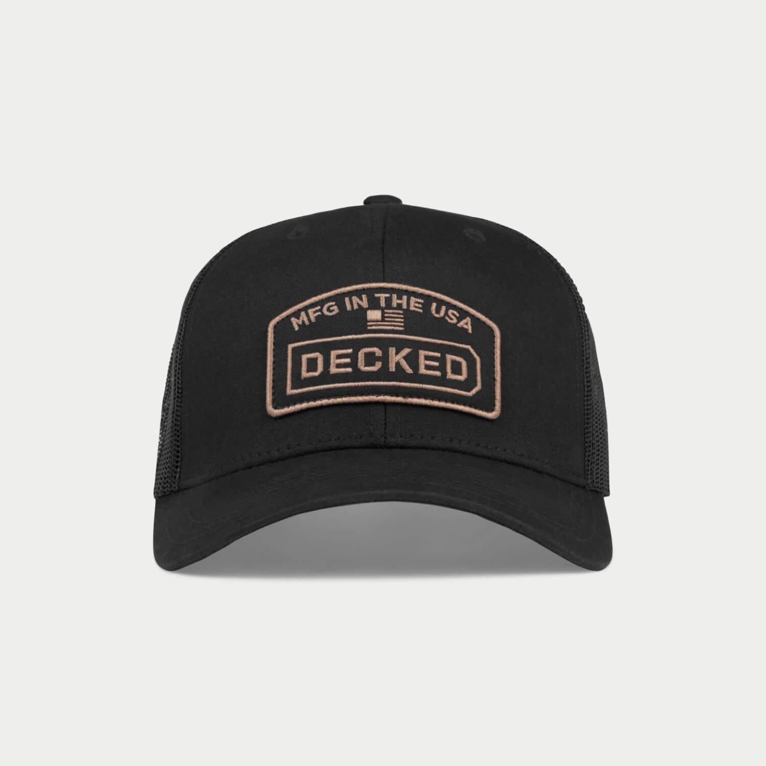 A black hat with a mesh back with a badge on it that has an embroidered "MFG in the USA", American Flag, and DECKED logo.