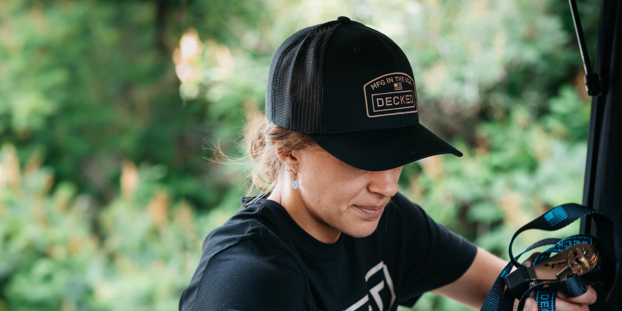 Person wearing a black cap and t-shirt with a DECKED logo, standing outdoors with greenery in the background