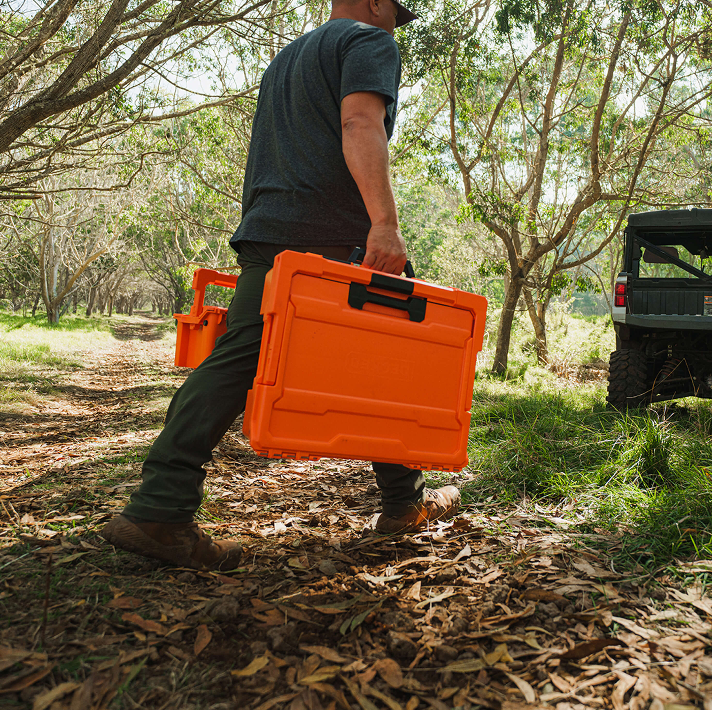 A man carrying two Blaze Orange D-co cases back to his side-by-side.