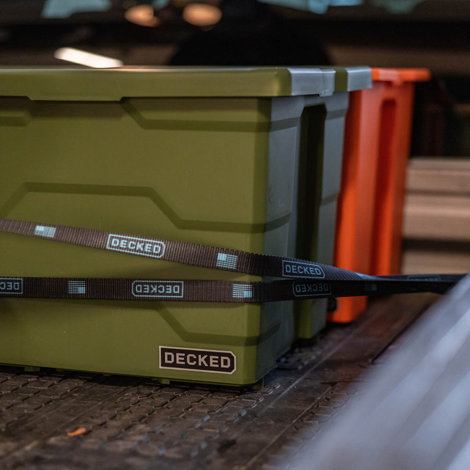 Green Payloader storage bin lashed down with a black ratchet strap to a truck bed.
