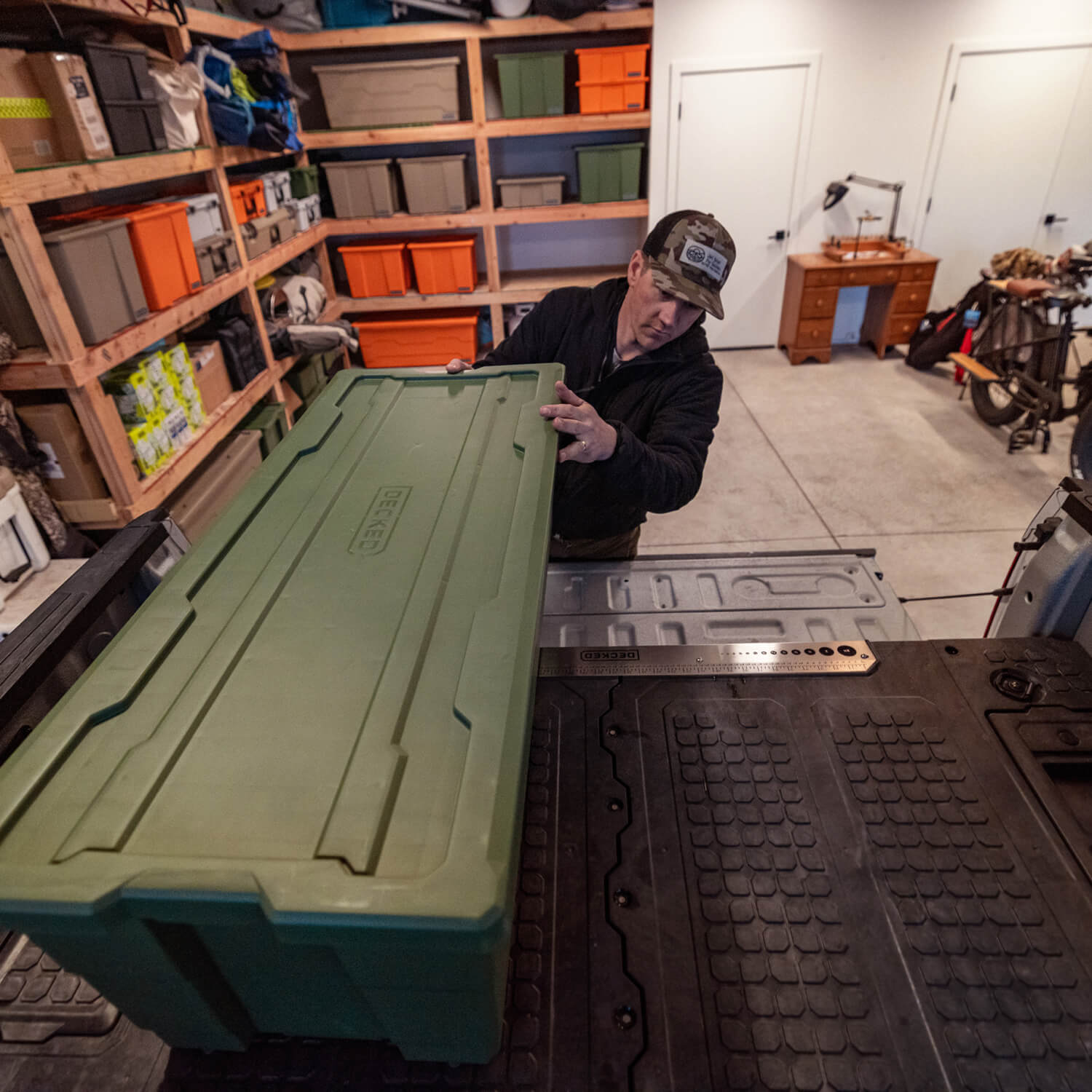 Man putting a large green Payloader 133 storage container into a truck bed in a workshop setting.