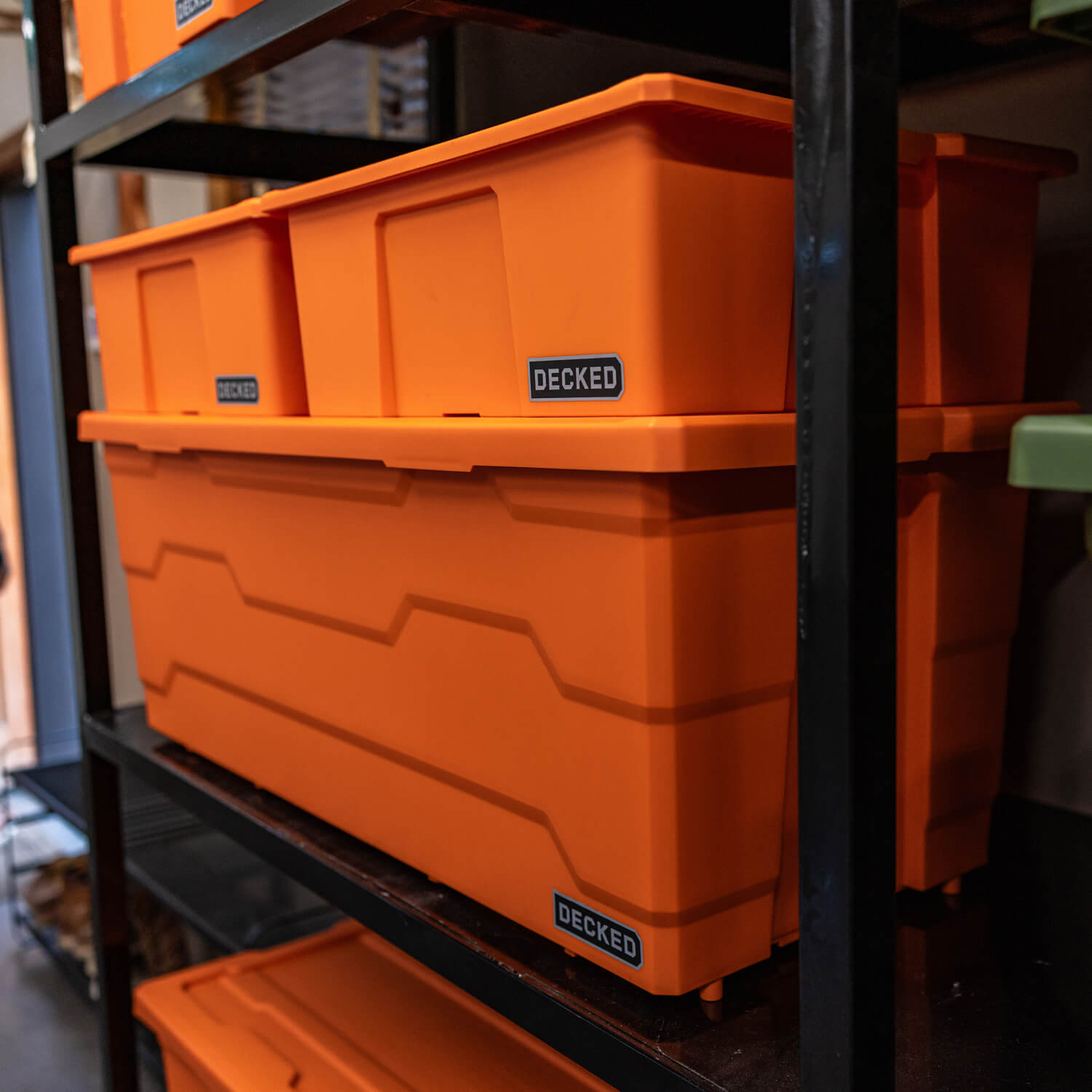 Stack of orange Payloader storage bins with 'DECKED' branding on a metal shelf.
