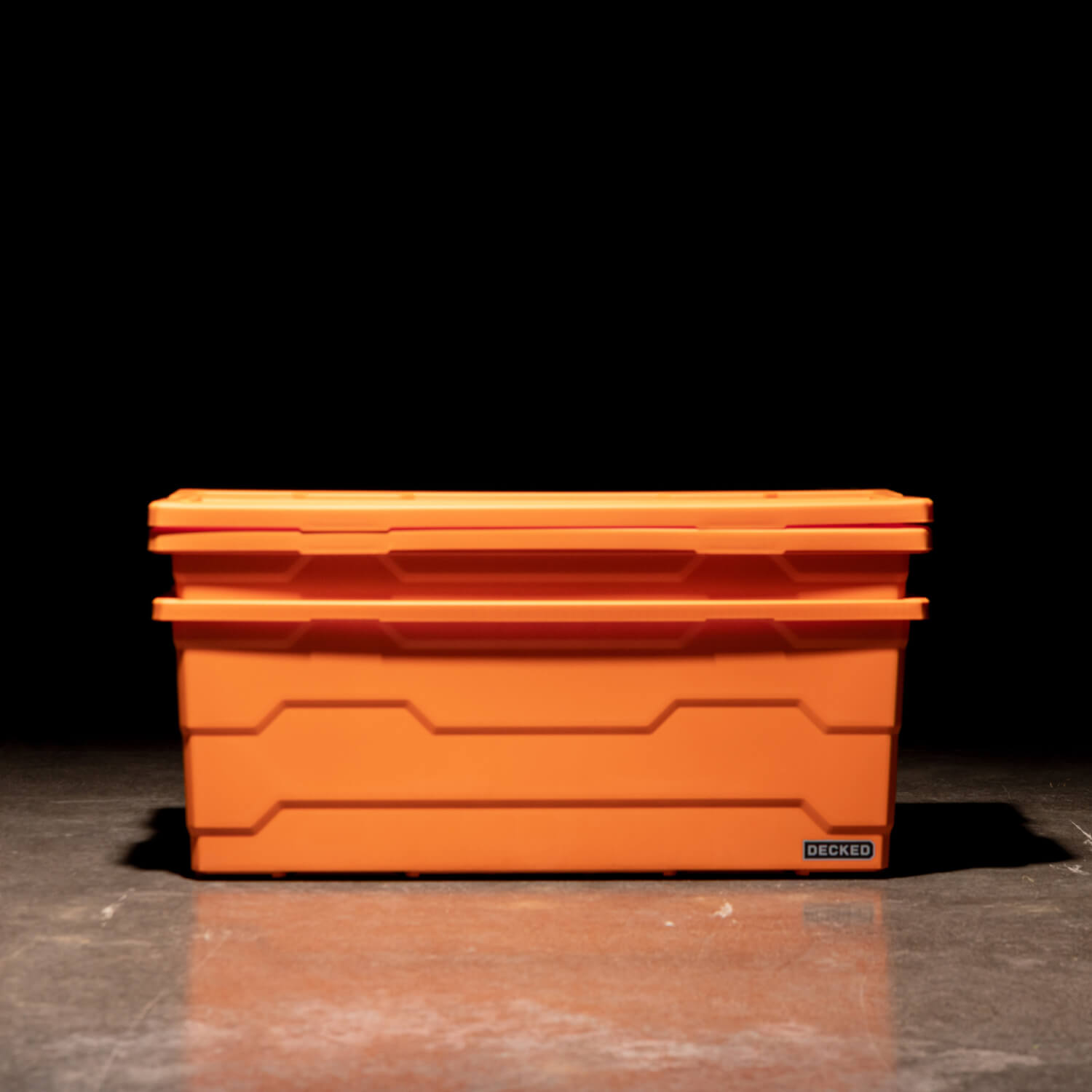 Two blaze orange Payloader 133 Bins nested together with the lids sitting on top in a garage with a dark, shadowy background.