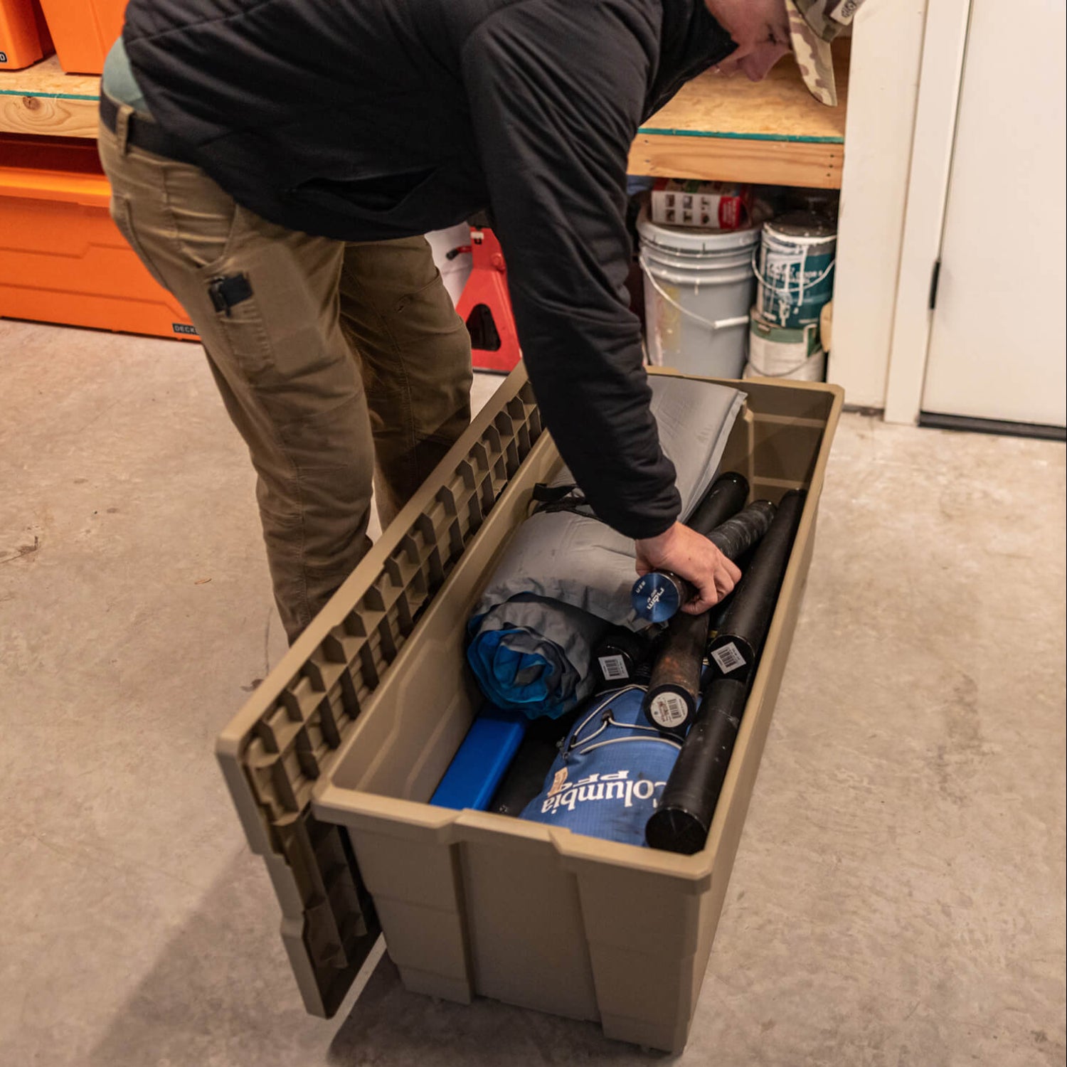 Person organizing sporting equiptment in a large Payloader 133 storage bin in a garage.