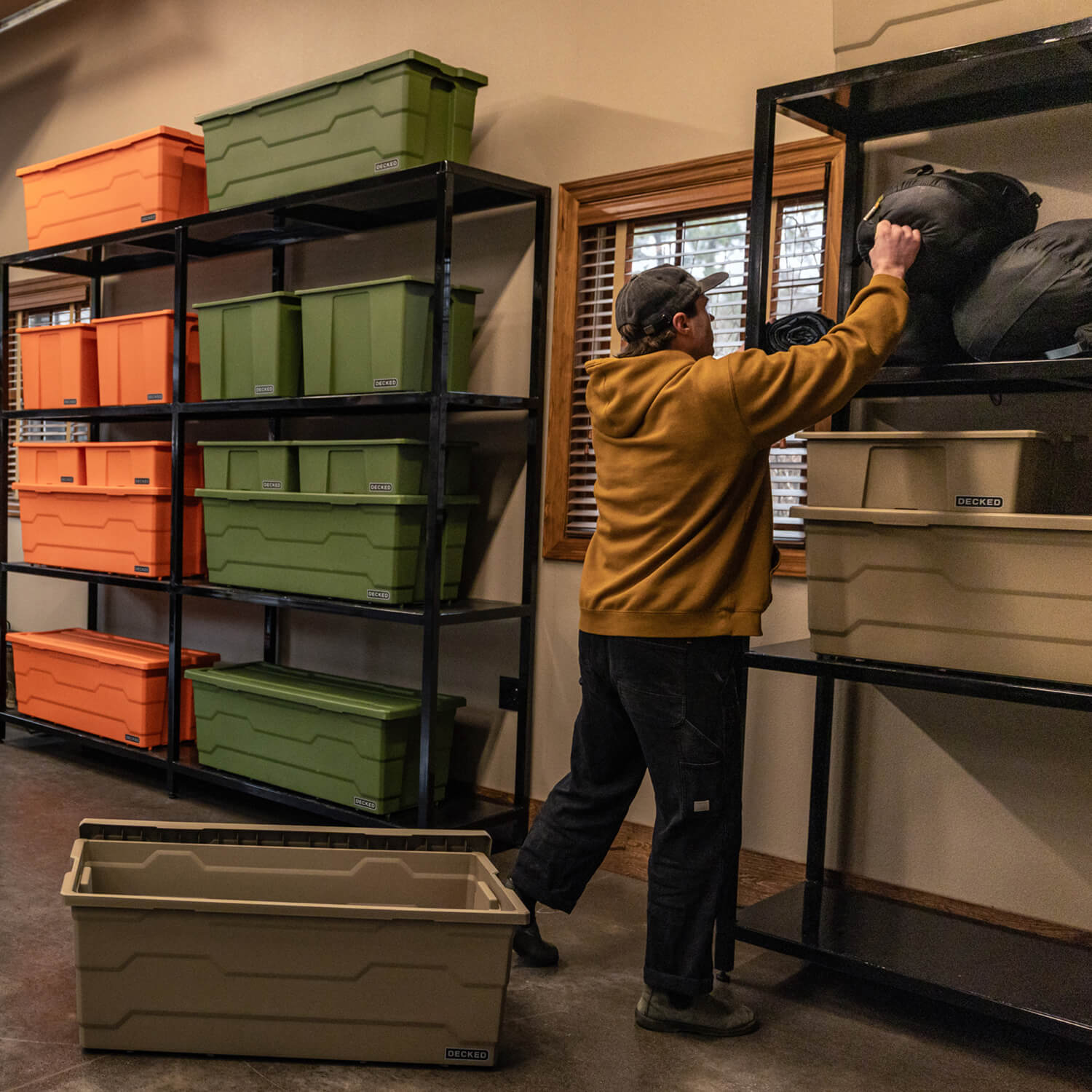 Person organizing Payloader storage bins in a garage with shelves and windows.