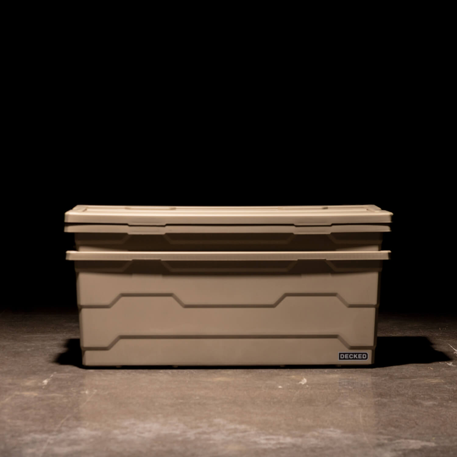 Two desert tan Payloader 133 Bins nested together with the lids sitting on top in a garage with a dark, shadowy background.