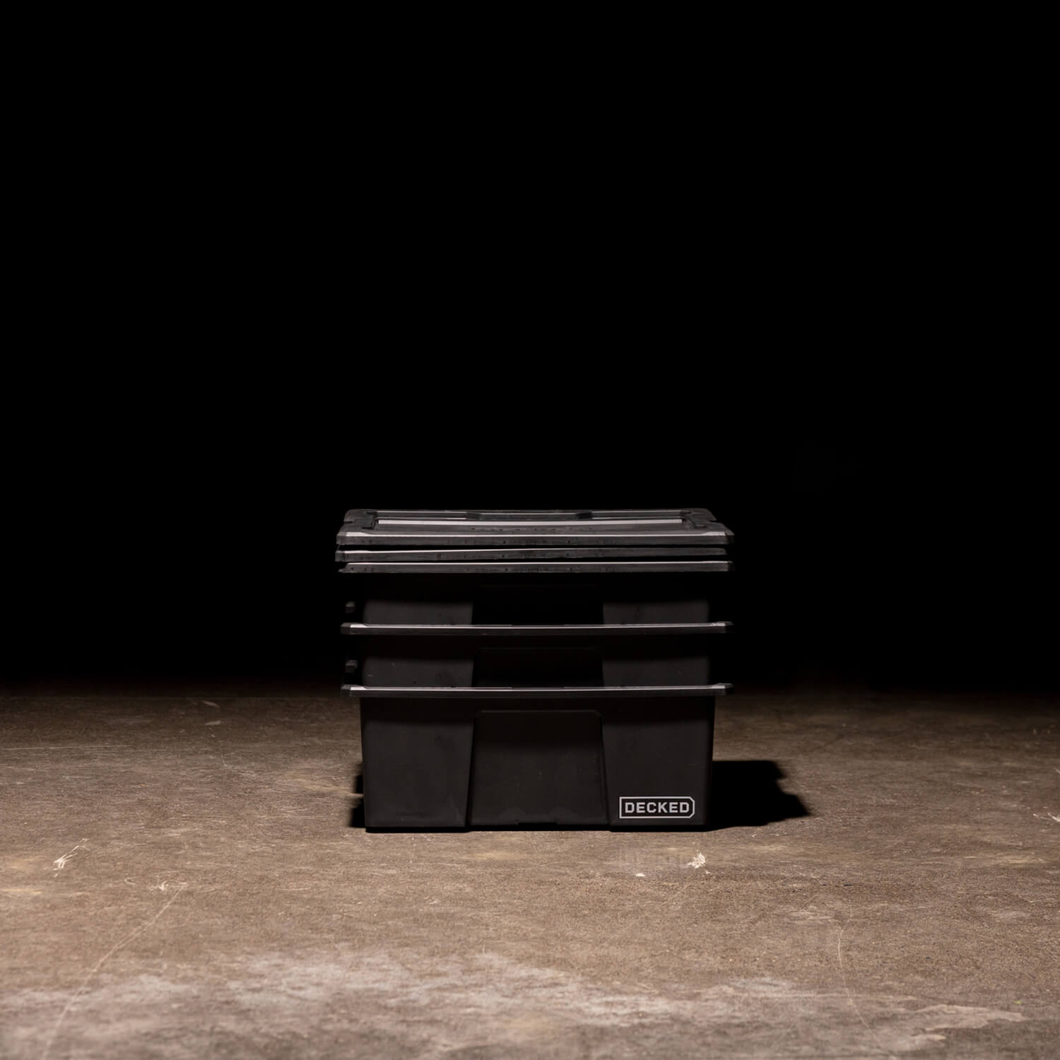 Three black Payloader Bins nested together with the lids sitting on top in a garage with a dark, shadowy background.