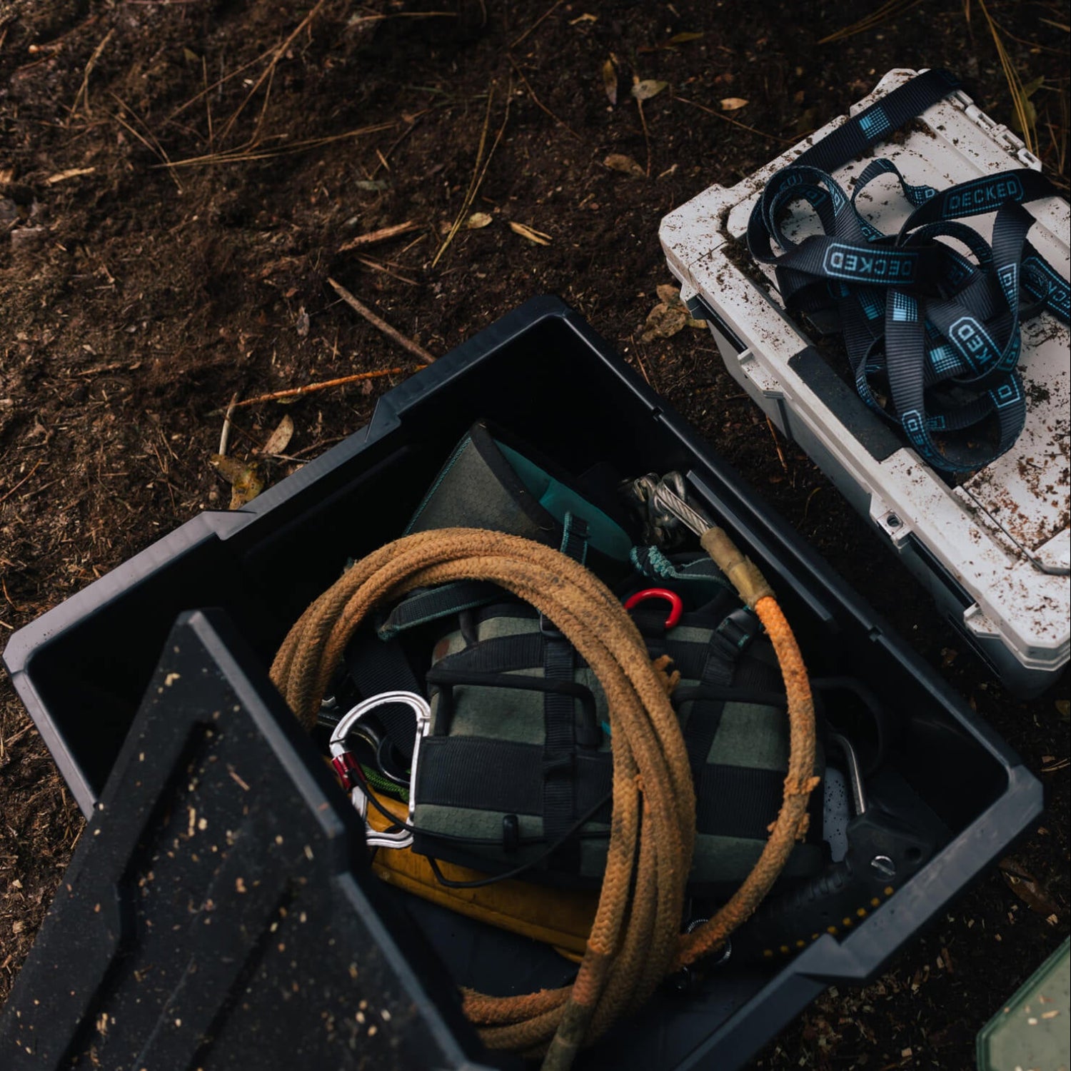 Saddle hunting gear inside of a black Payloader Bin on a forest floor.