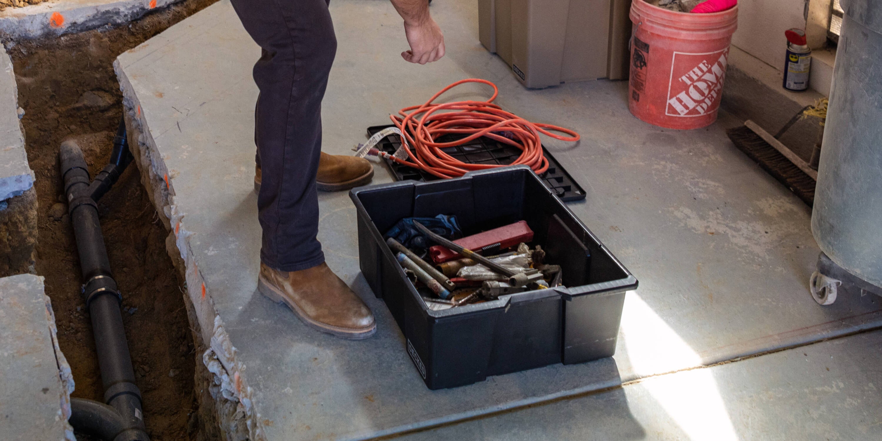 A man at a jobsite retrieving tools and extension cords from a black Payloader Bin.