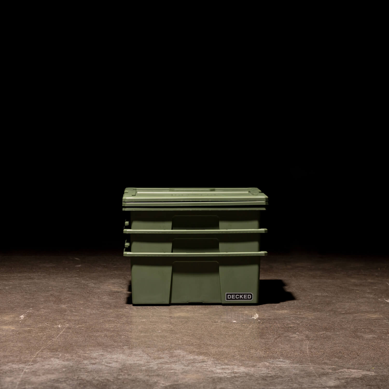 Three ranger green Payloader Bins nested together with the lids sitting on top in a garage with a dark, shadowy background.