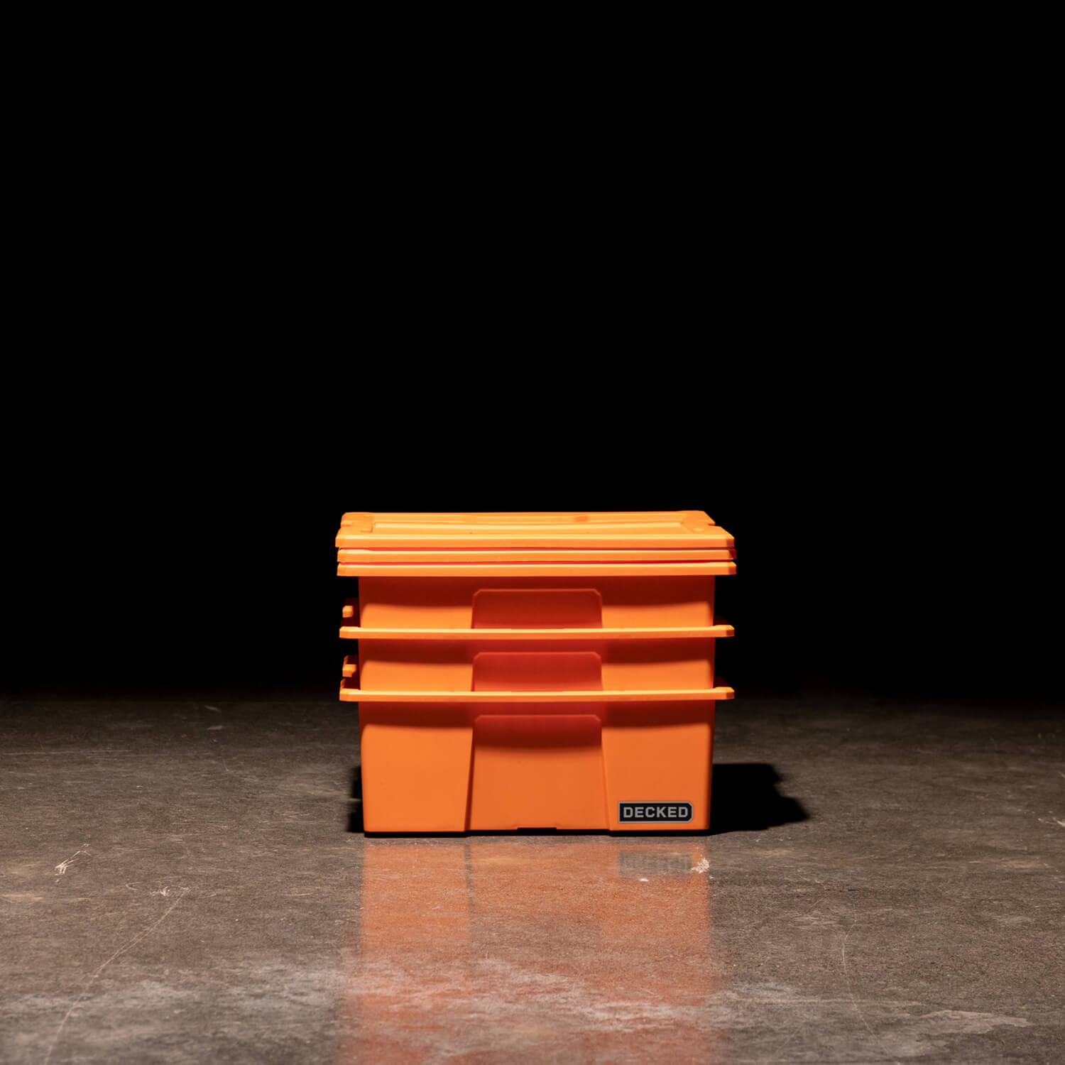 Three blaze orange Payloader Bins nested together with the lids sitting on top in a garage with a dark, shadowy background.