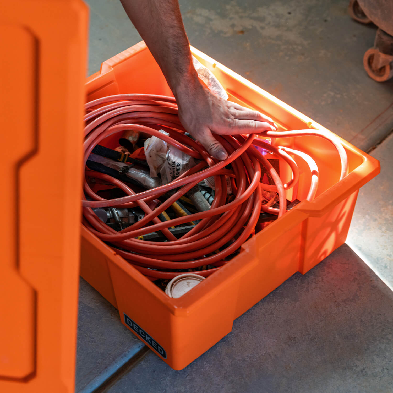 A man placing an extension cord and other small tools in his blaze orange Payloader Bin.