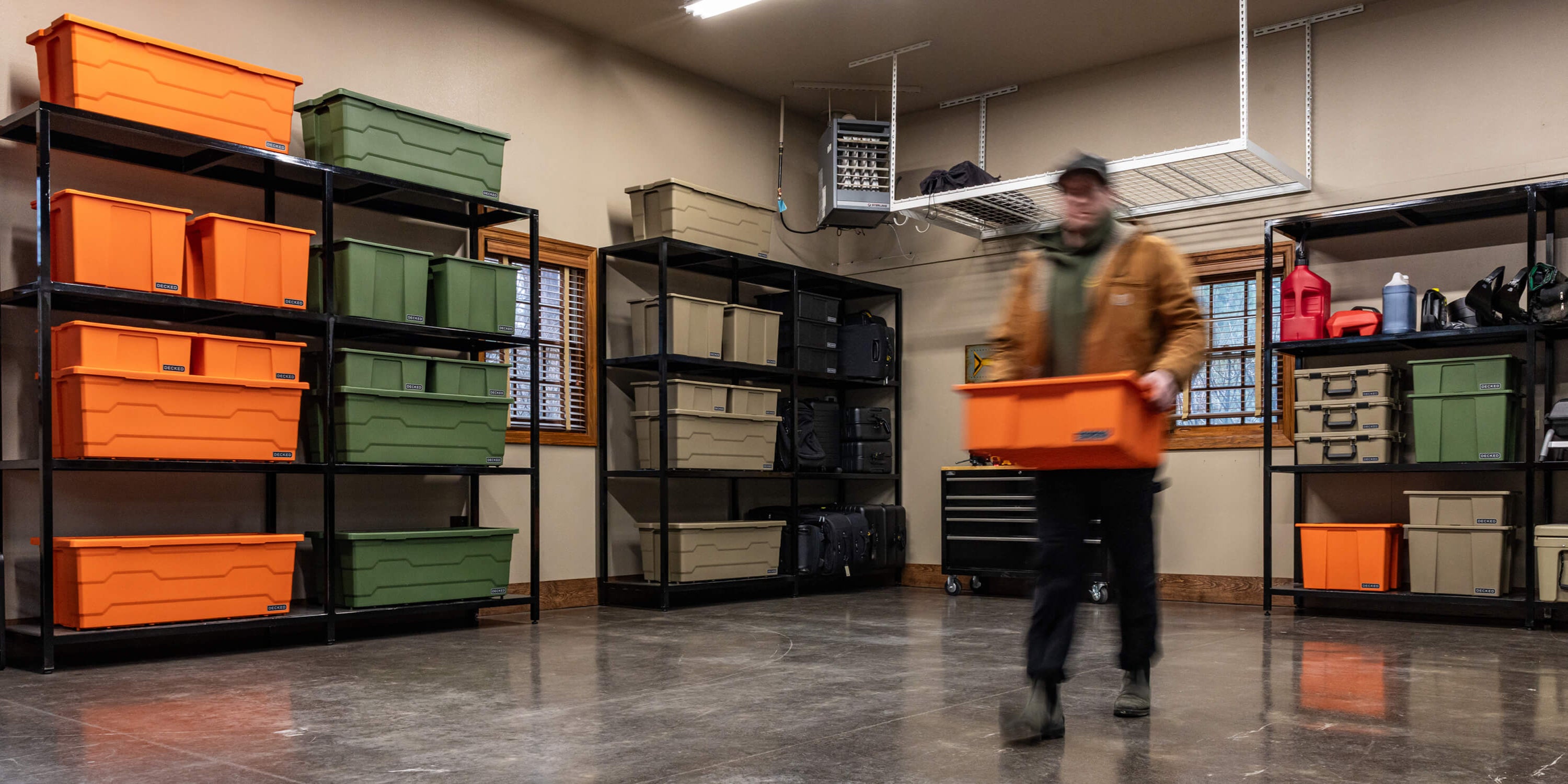 A man carrying a blaze orange Payloader Bin from a storage bin in his garage to his vehicle.