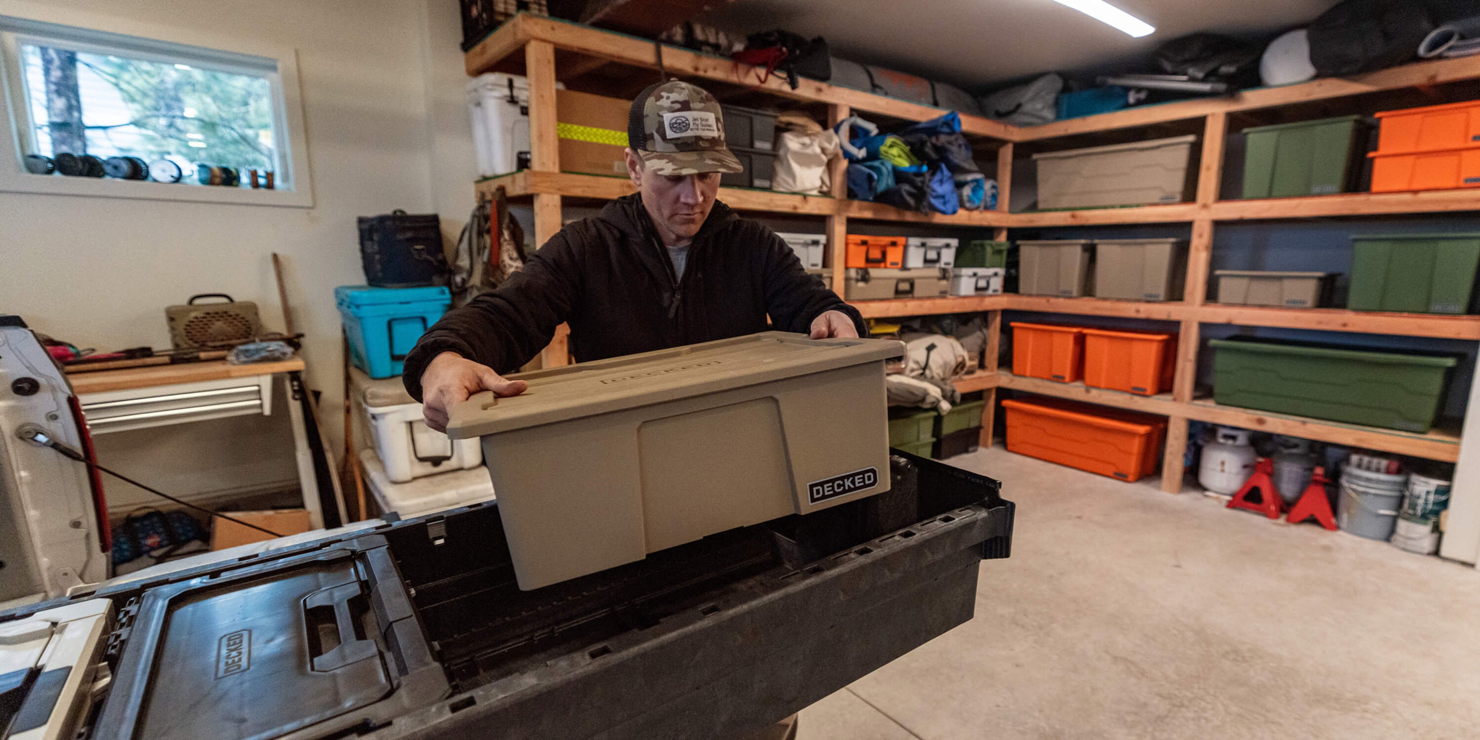 A man loading a single desert tan Payloader Bin into a DECKED Drawer System in his garage.