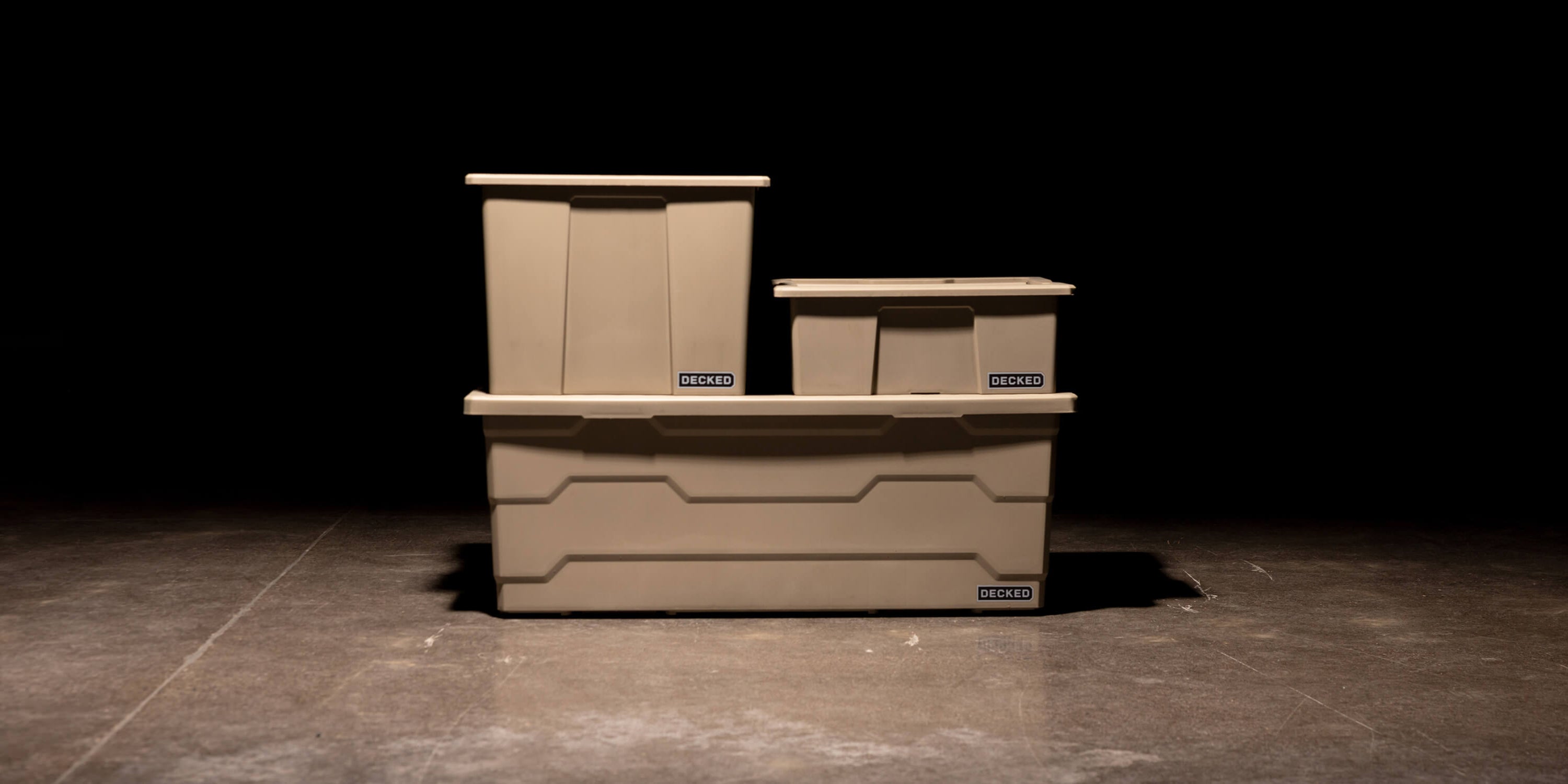 Three desert tan Payloader Bin sizes stacked on top of each other in a garage with a dark, shadowy background.