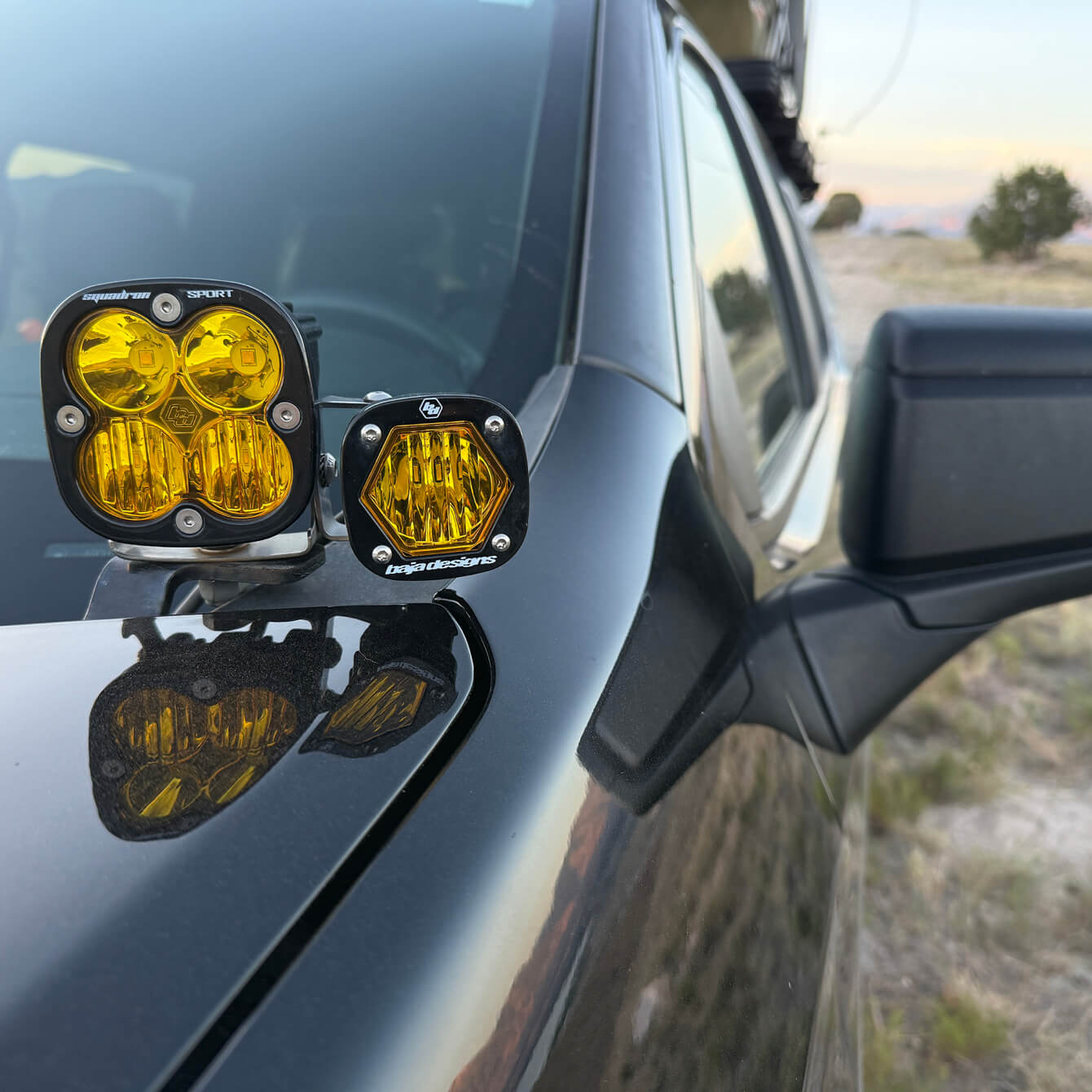 Yellow fog lights mounted on a car's side panel with a desert landscape in the background.