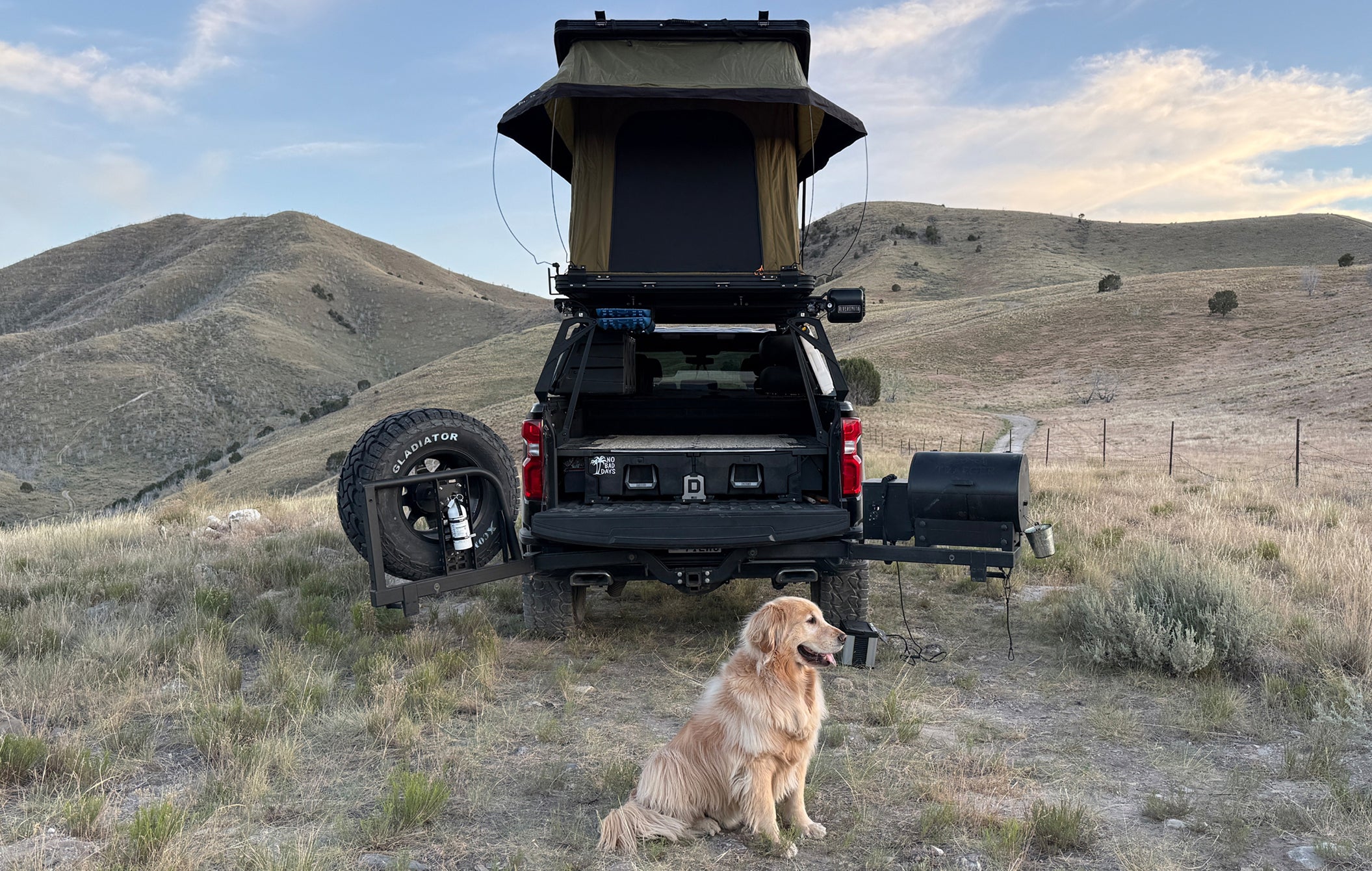 Black SUV with a rooftop tent in a desert landscape with a dog sitting in front.