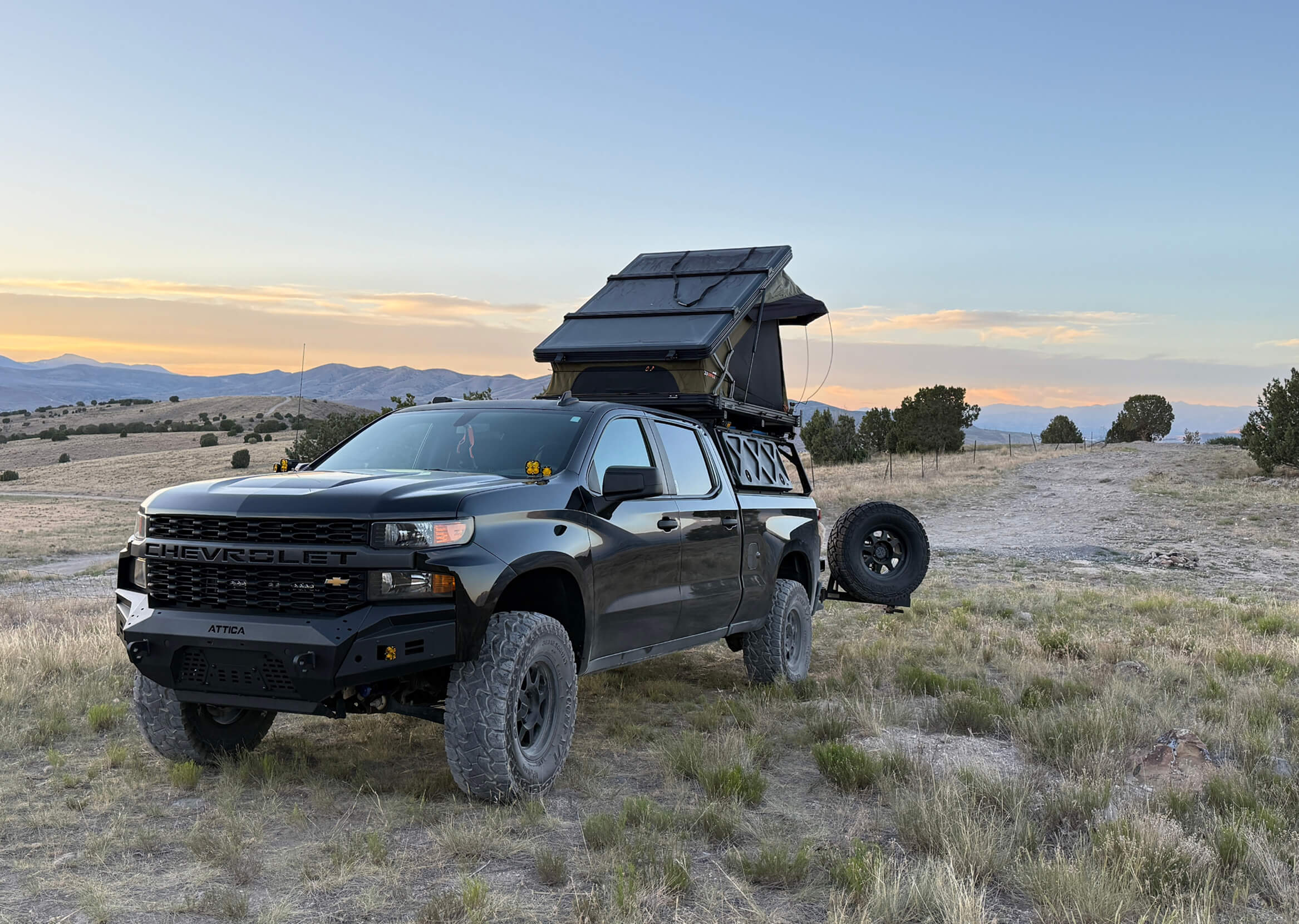 Black truck with a roof tent in a desert landscape at sunset