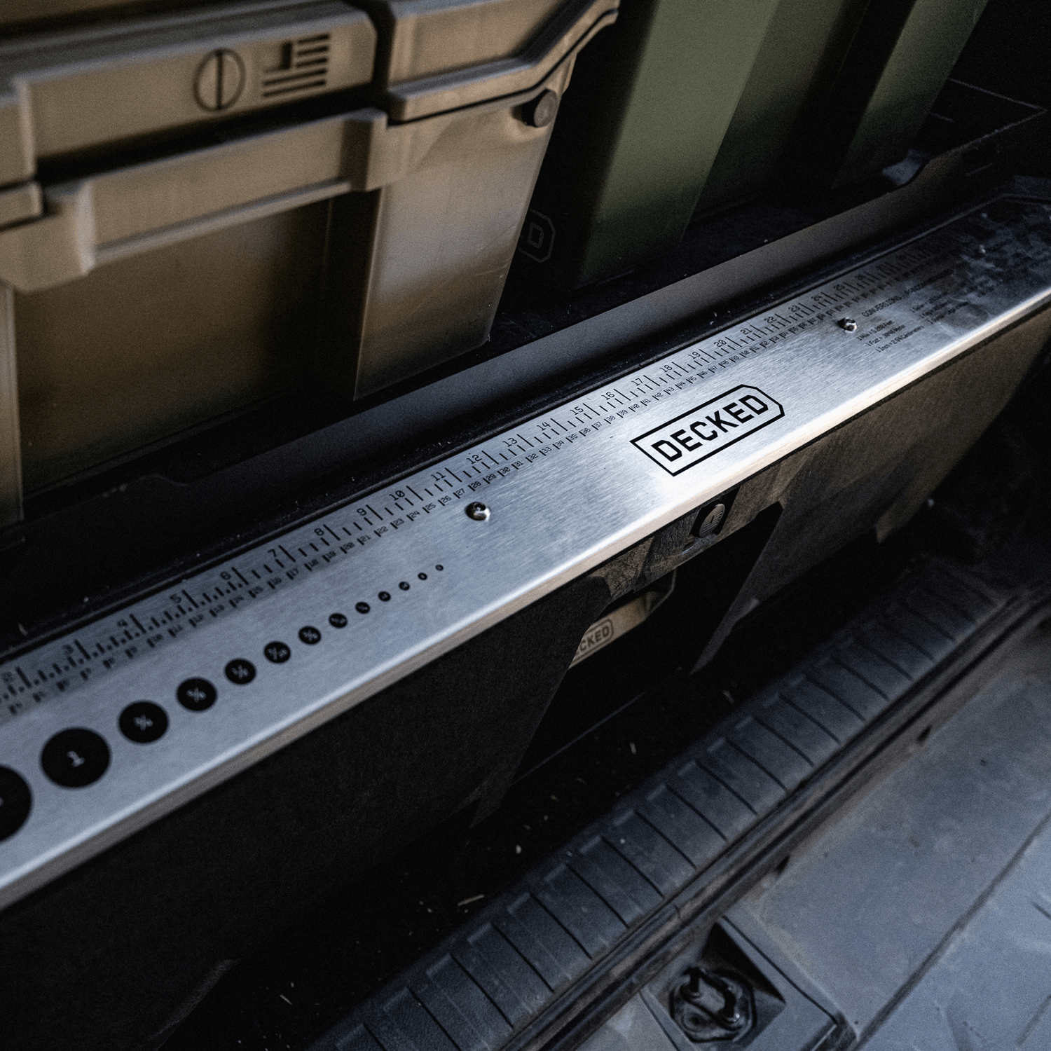 Close-up of a stainless steel deck rail with a black 'DECKED' logo patch, showing measurement markings installed on the DECKED Drawer System.