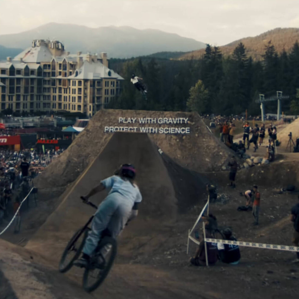 Casey performing a stunt on a dirt ramp with a building and trees in the background, featuring the text 'Play with Gravity. Protect with Science'.