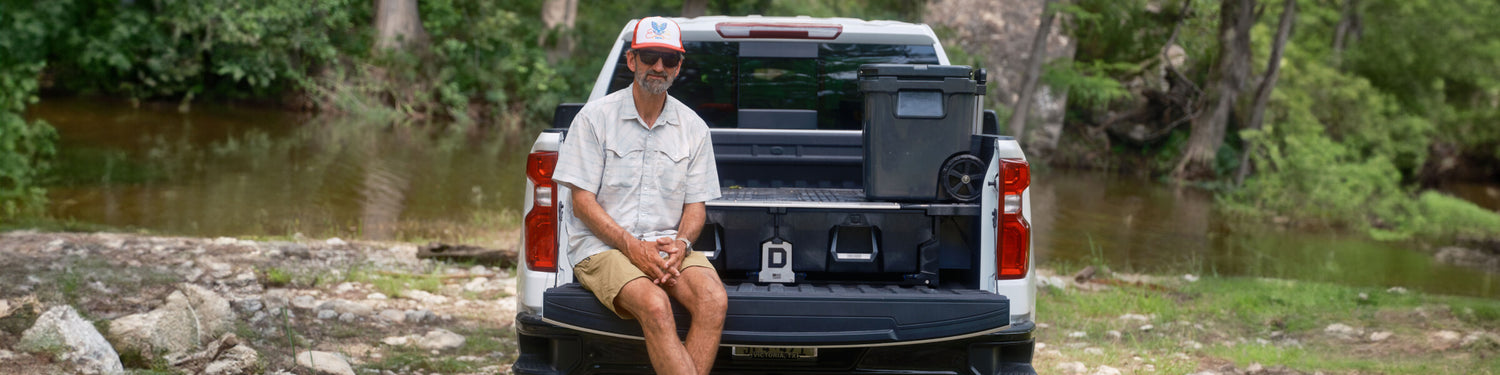 JT VanZant sitting on his tailgate in front of his DECKED Drawer System by a river.