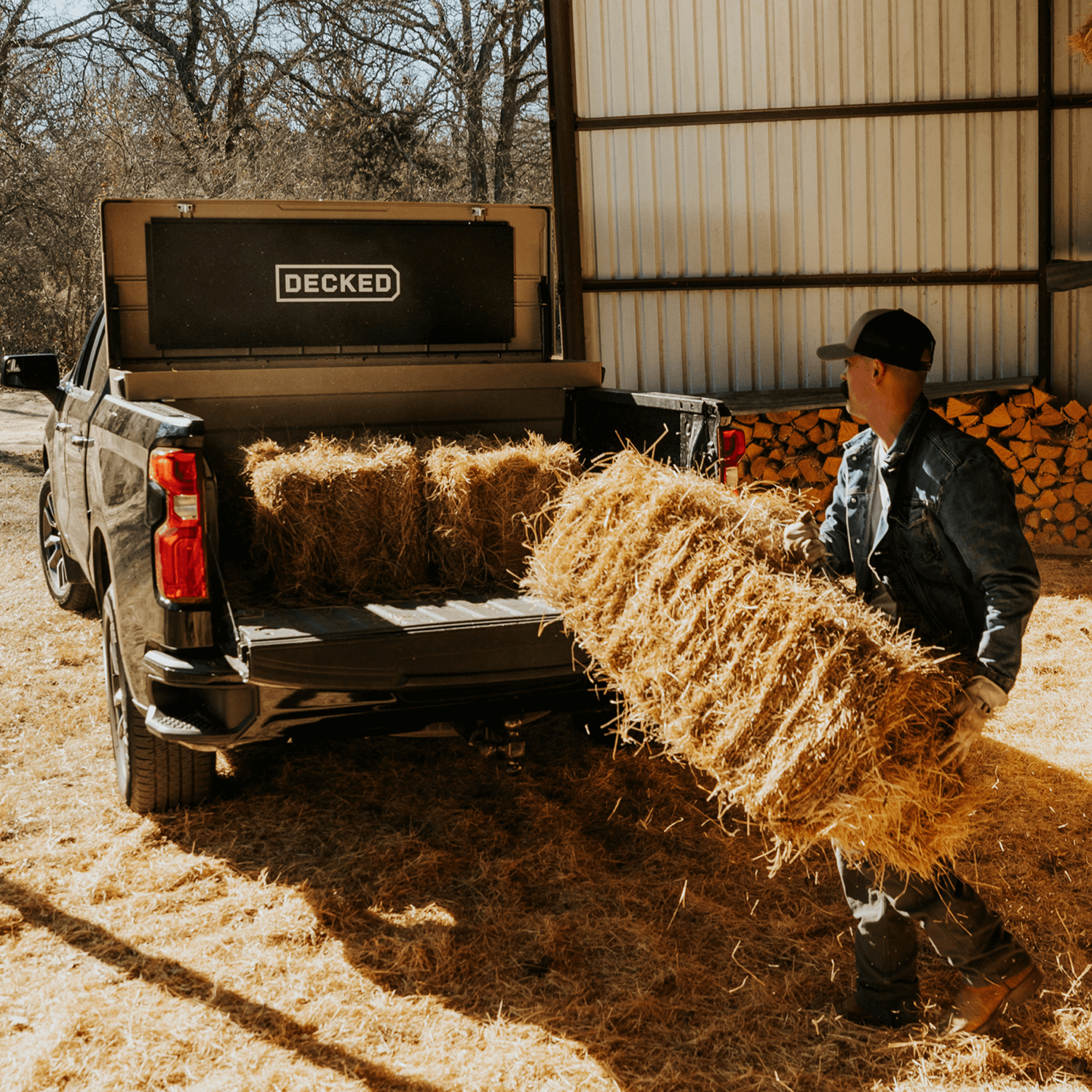Person loading hay bales into a truck with 'DECKED' Tool Box in the bed.