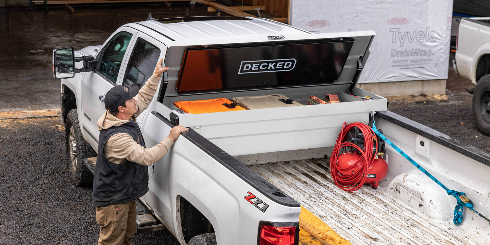 Person closing the white DECKED Tool Box in his truck bed at a construction site.