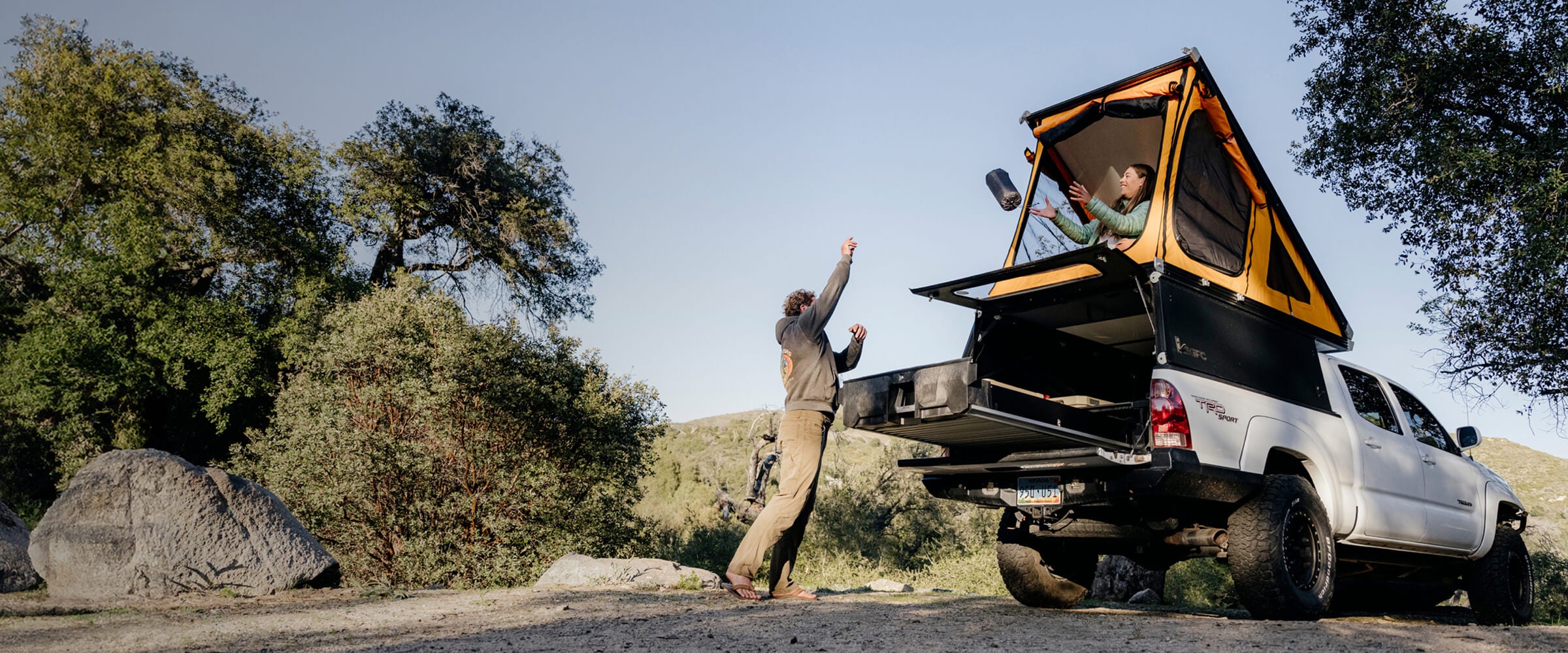 Two people tossing a sleeping pad from their Drawer System to their rooftop tent at their campsite.