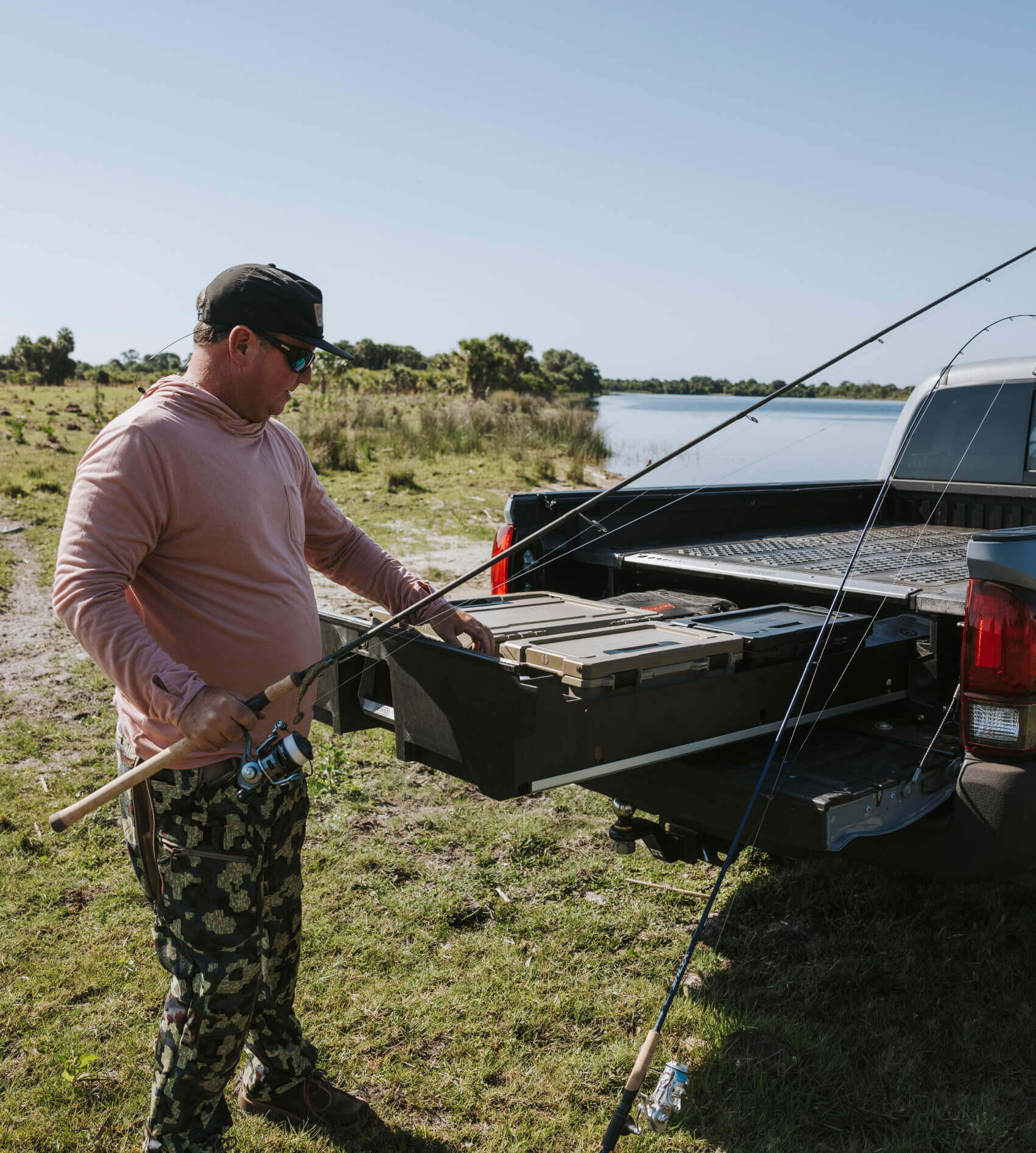 Man preparing fishing equipment in the back of a pickup truck with a DECKED Drawer System by a lake.