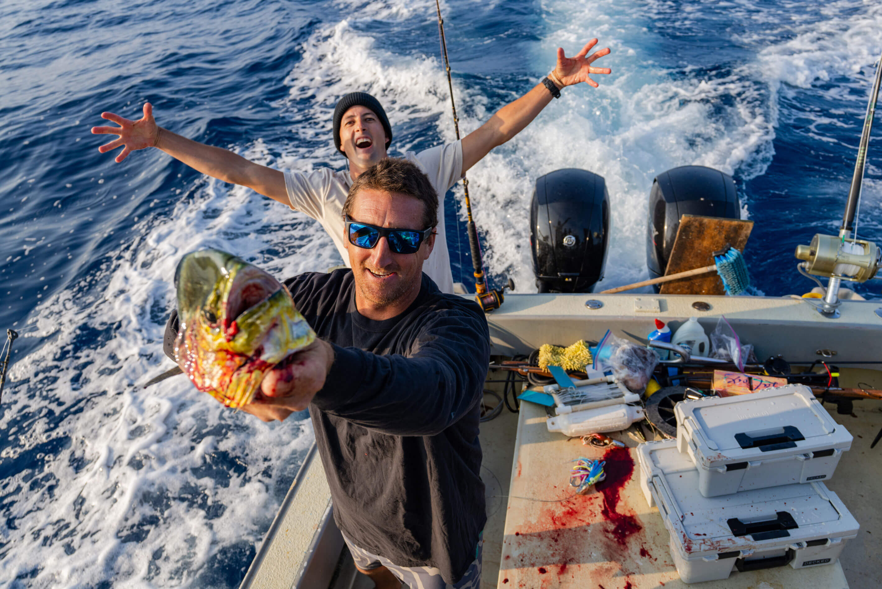 Two men on a boat with one holding a large fish, surrounded by ocean waves.