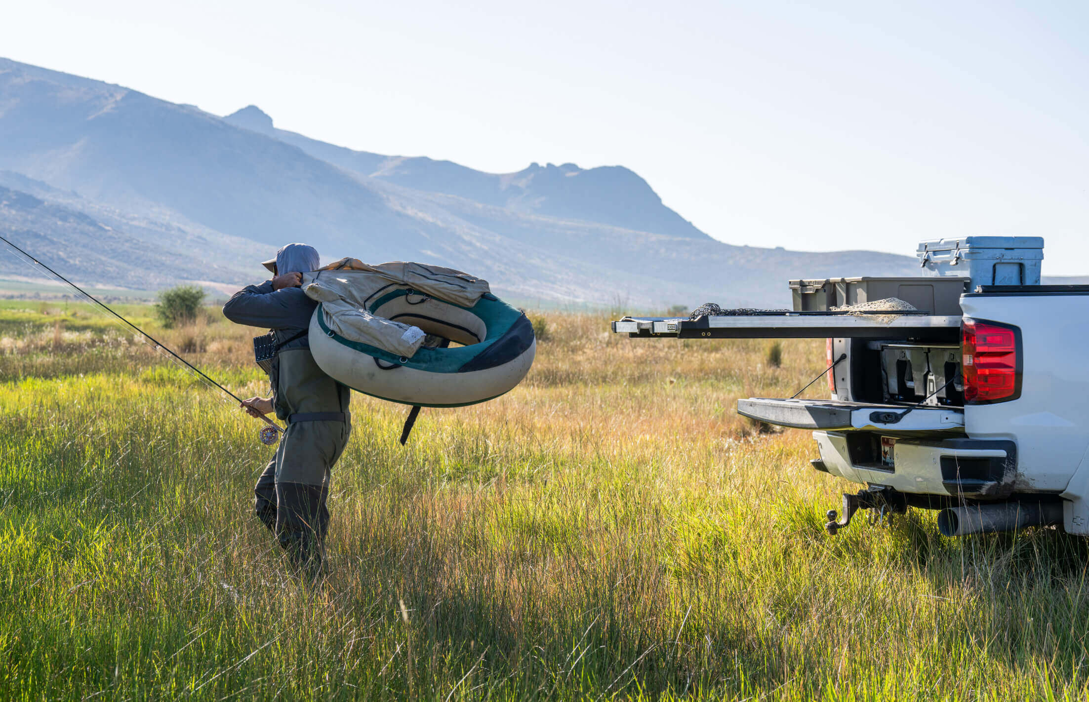 Person carrying an inner tube near a truck with a CargoGlide extended in a grassy field with mountains in the background