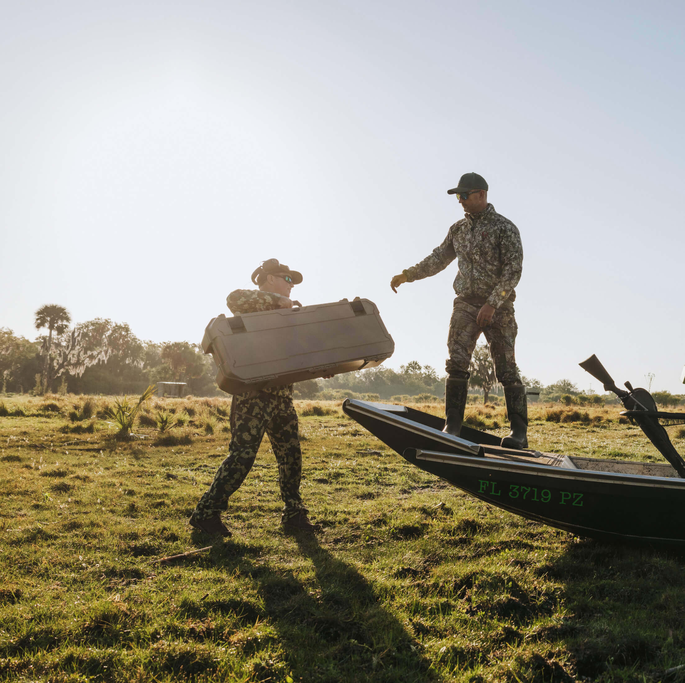 Two individuals in camouflage gear with a Honcho 80L D-co case and airboat.