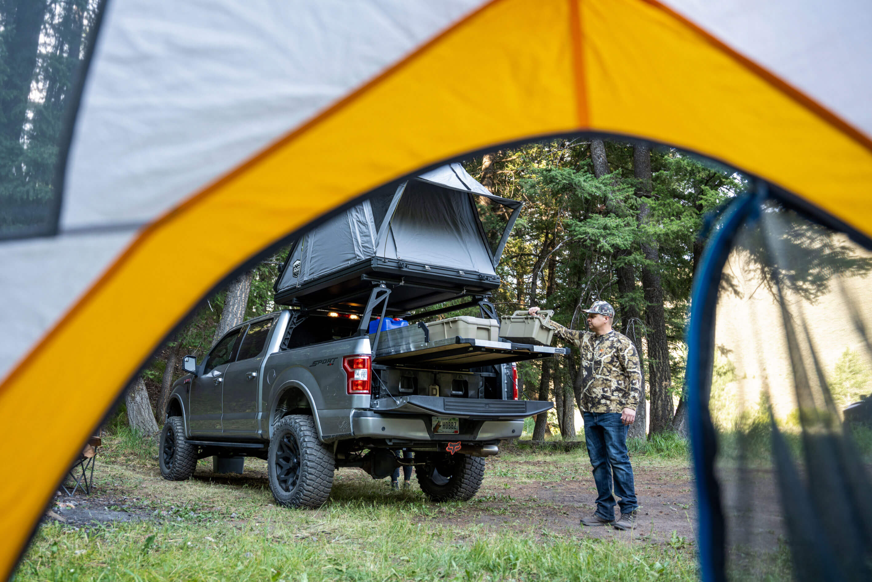 Person standing next to a truck with a Drawer System and rooftop tent at a campsite.
