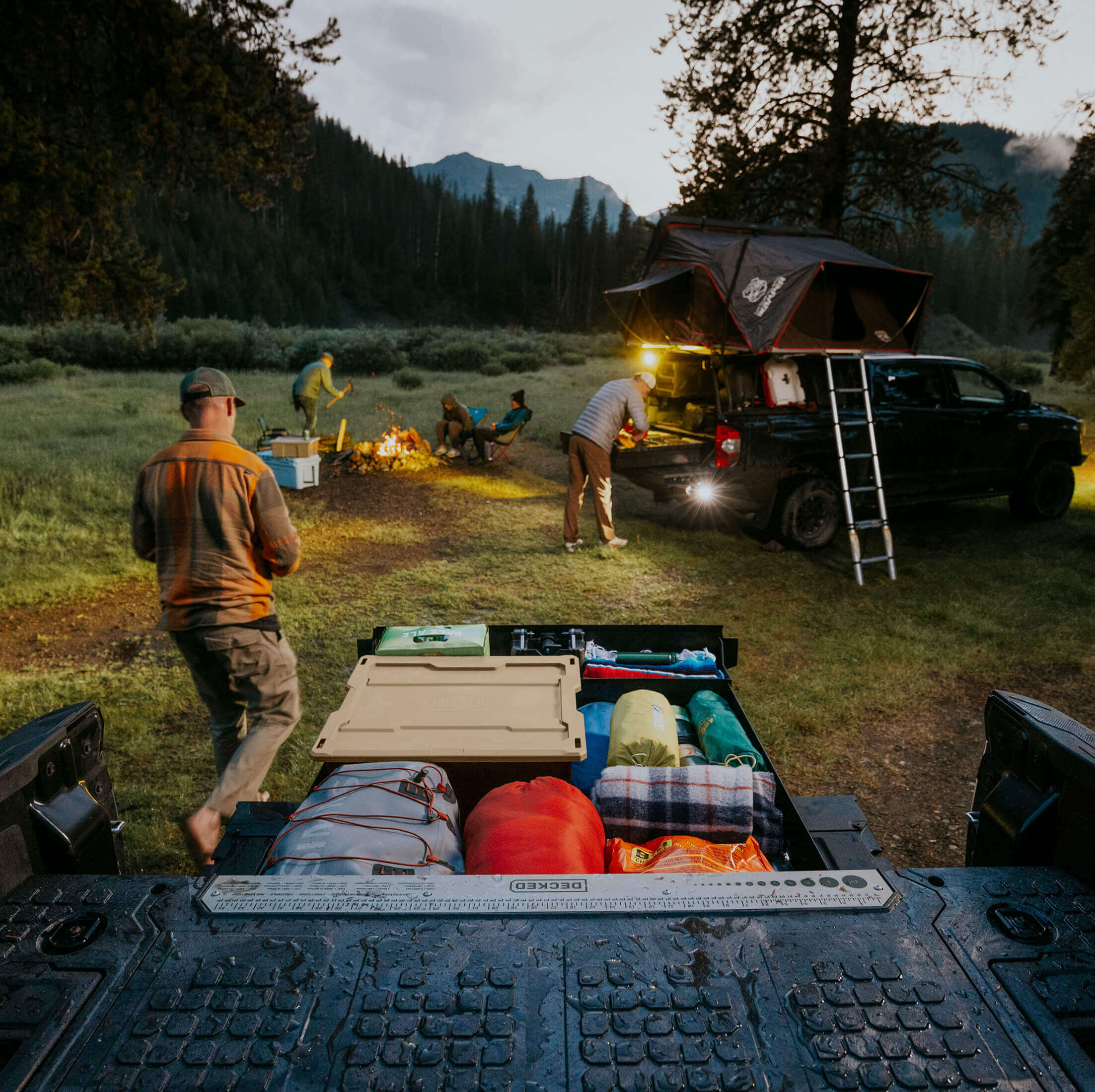 Group of people camping in a forest with trucks equipped with DECKED Drawer Systems and rooftop tents.