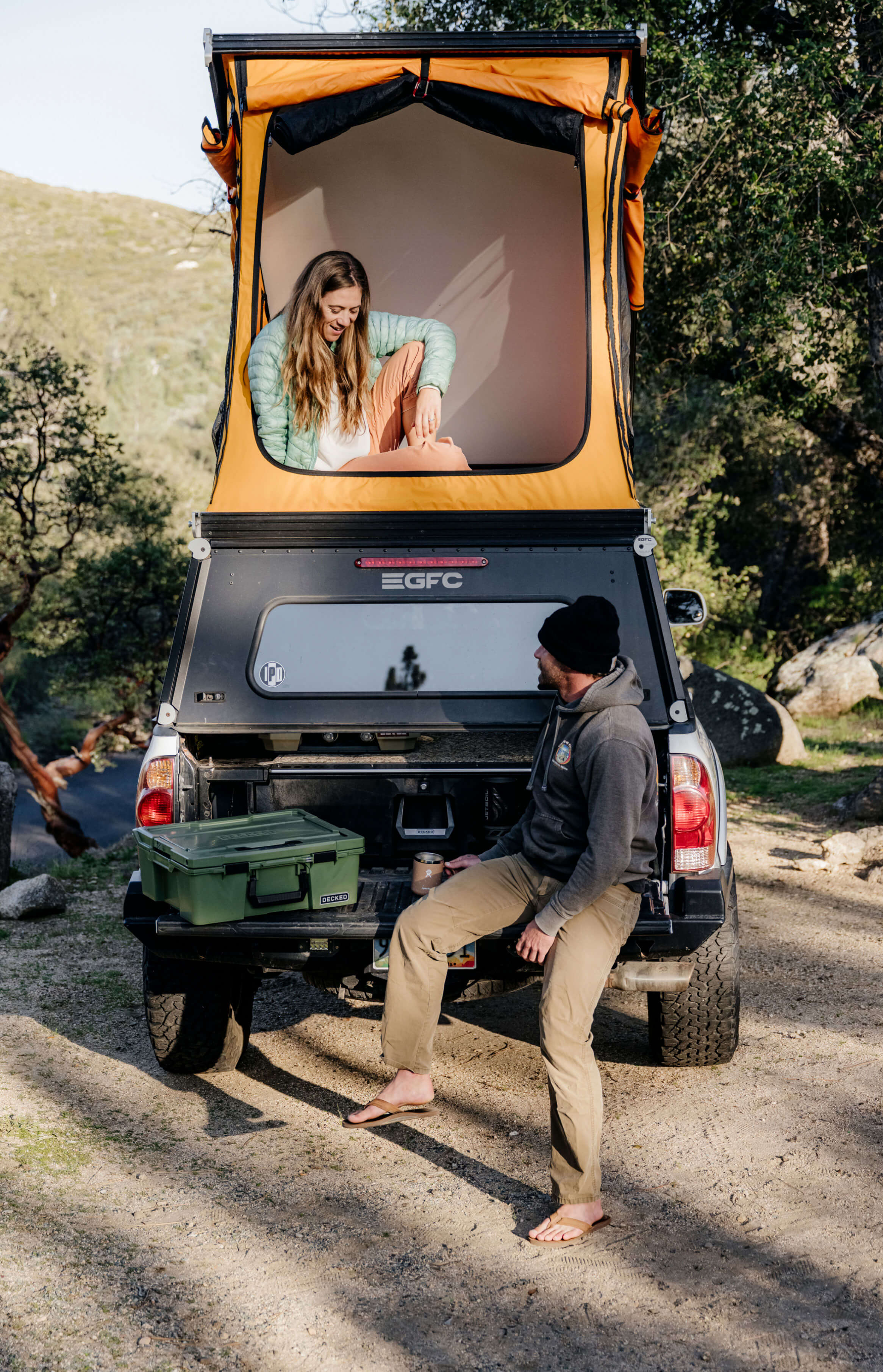 Two people by a truck with an open roof tent and a Drawer System in a natural setting.