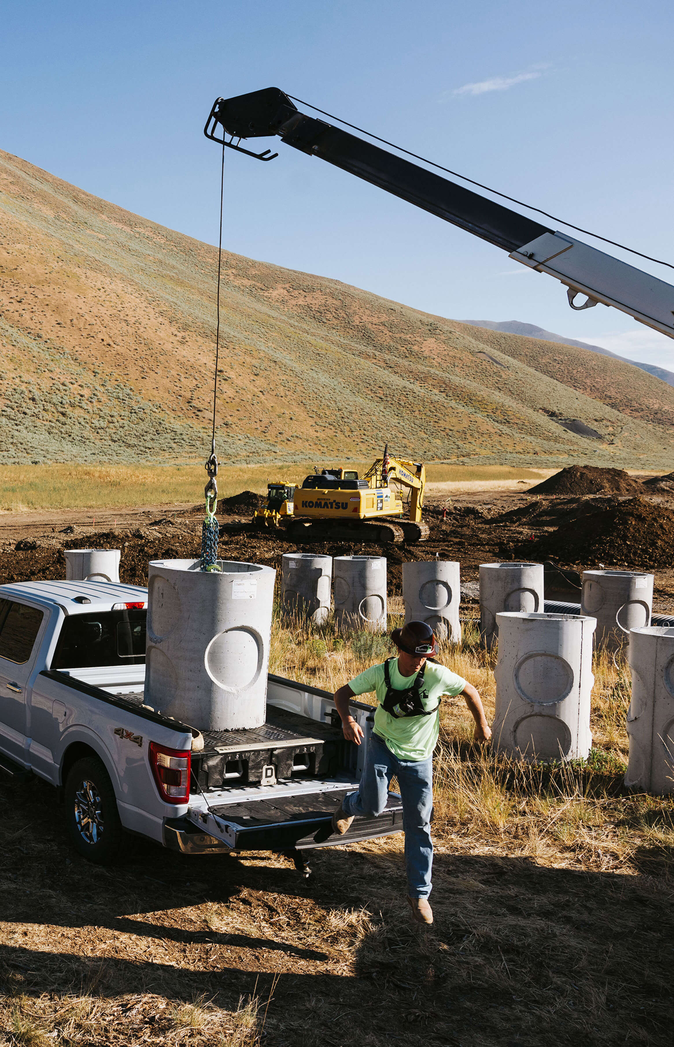 Person loading large cylindrical objects onto the deck of a Drawer System in a white truck with a crane in a desert-like setting.