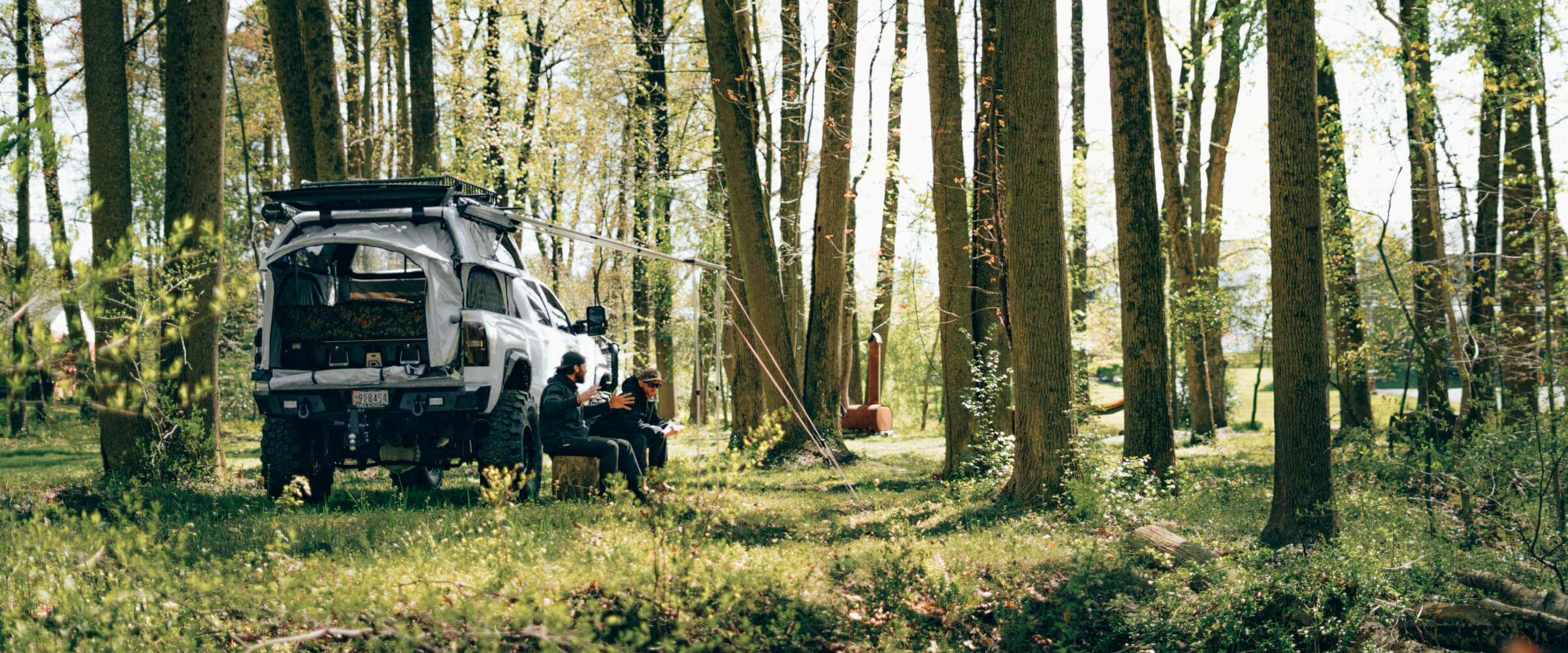 two people sitting next to a truck with a popup tent in the woods