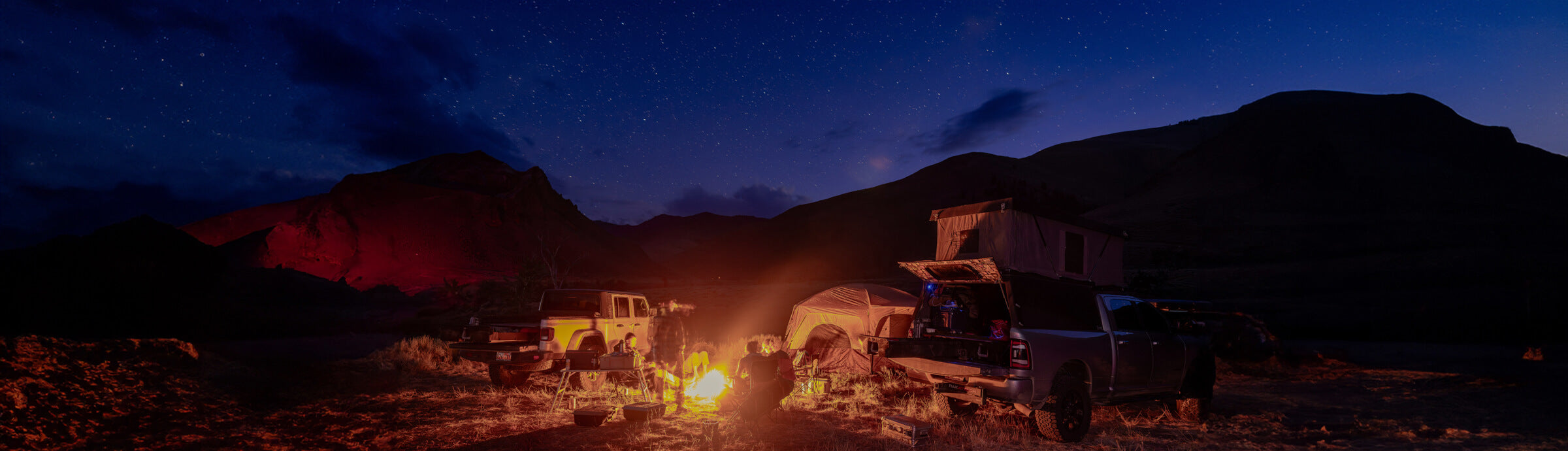 A group of friends truck camping around a campfire.