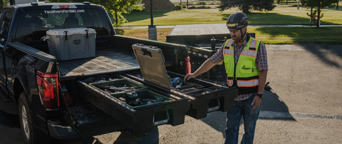 Worker accessing tools in open DECKED drawers, with a Payloader case on the truck bed deck.