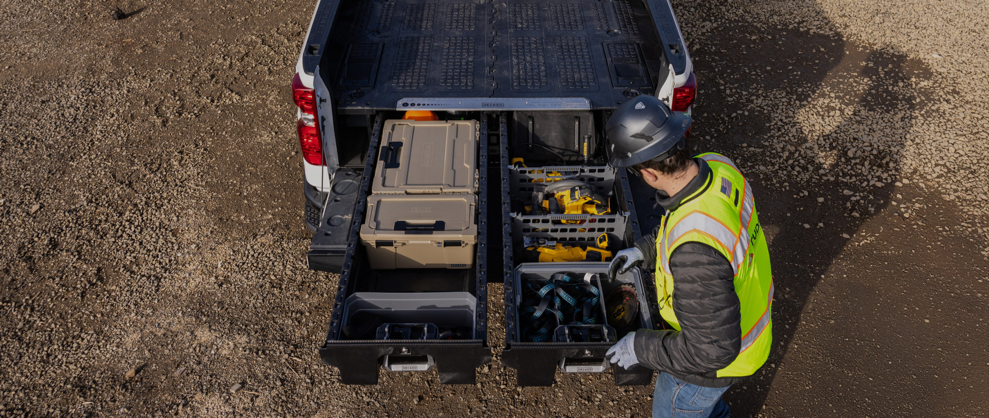 Person in high-visibility vest and hard hat interacting with toolboxes in a truck bed.