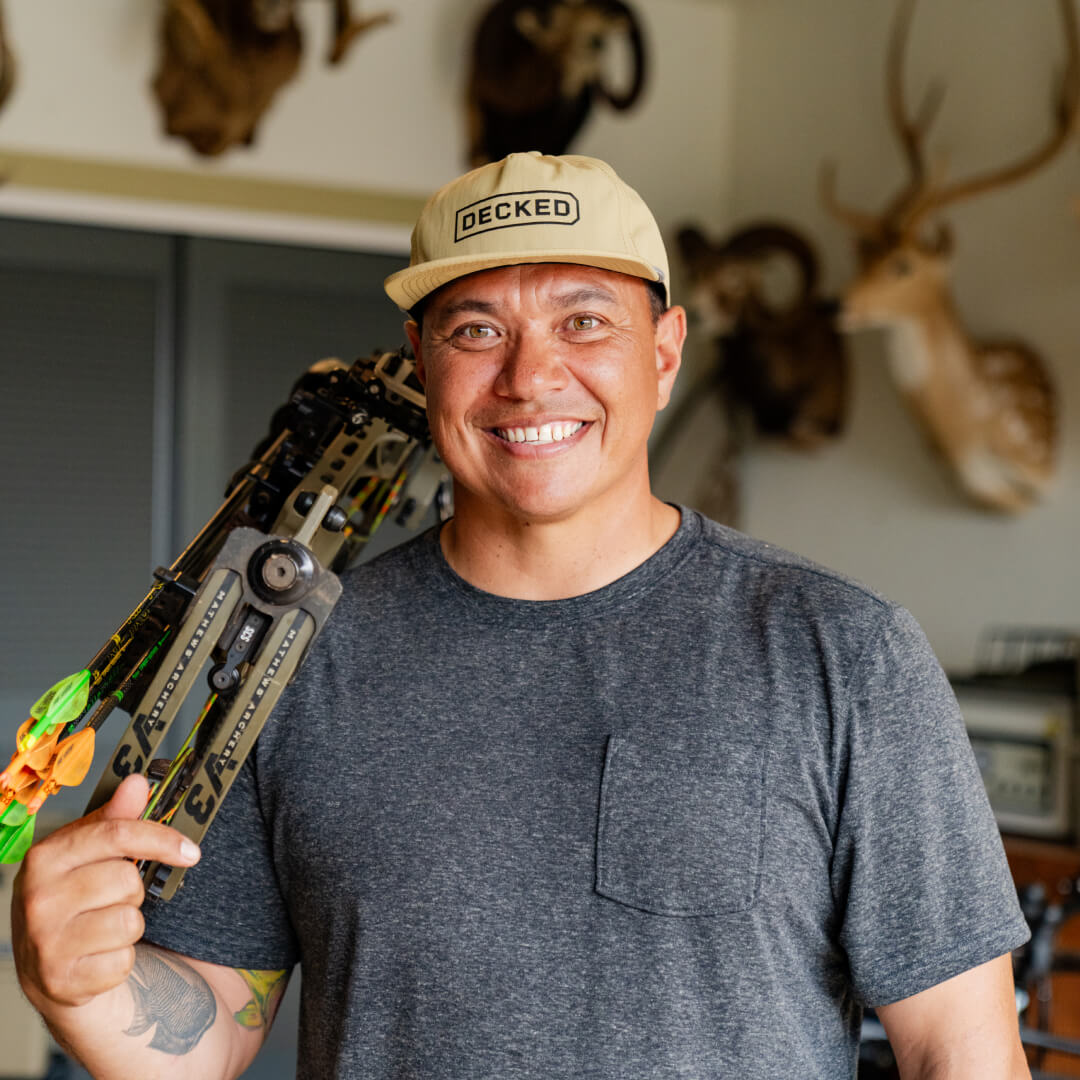 Justin Lee in his garage in a DECKED hat with his bow over his shoulder.