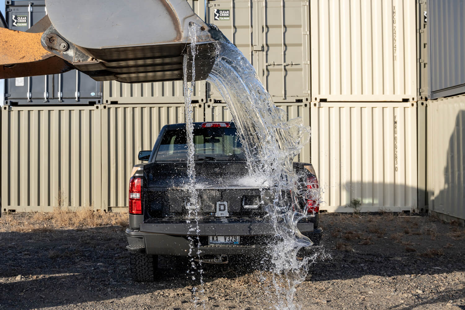 Bulldozer dumping water onto a DECKED drawer system in the bed of a Ford truck to demonstrate waterproof protection.